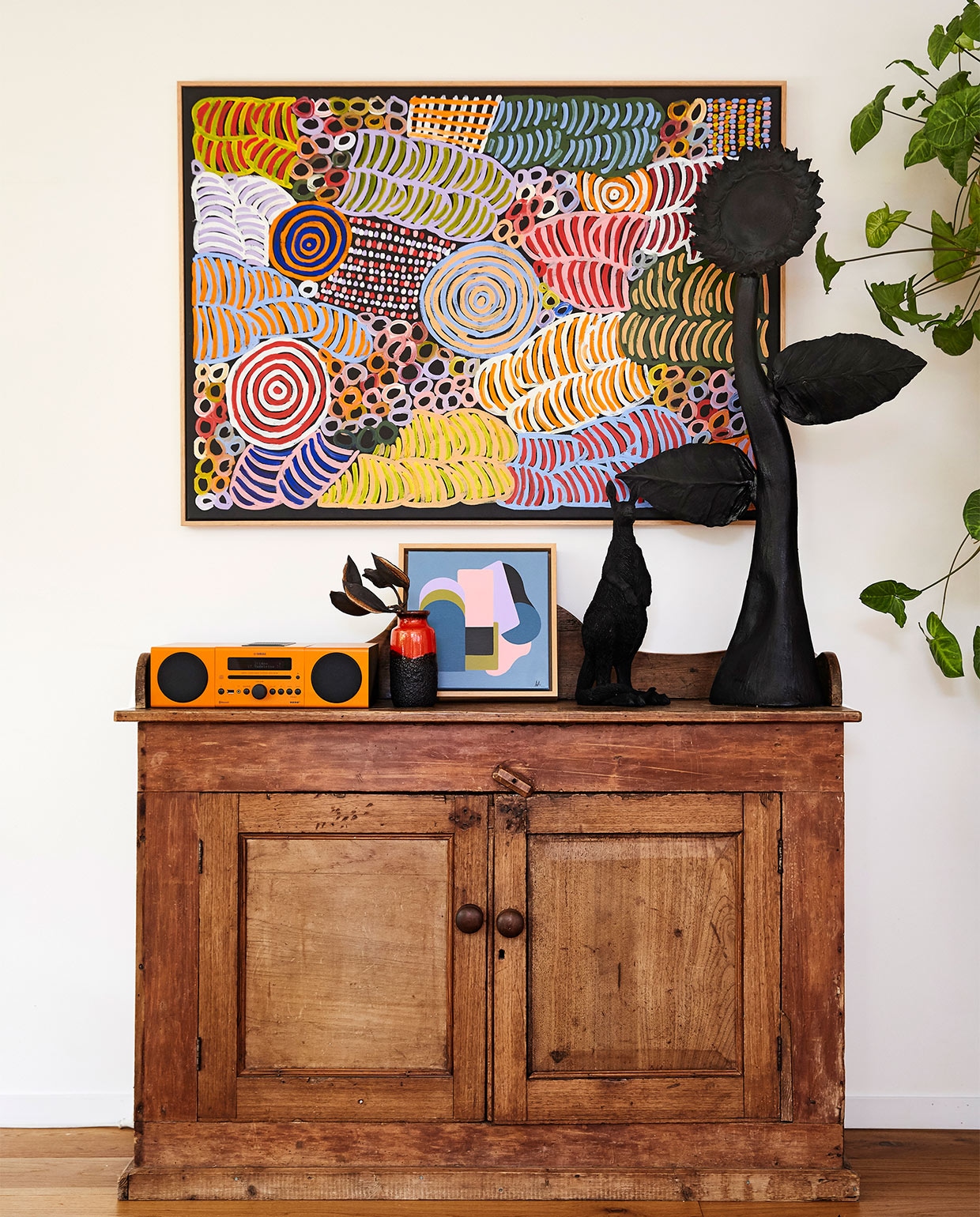 Antiek dressoir gekregen van Madeleines moeder. Schilderij van Betty Mbitjana. Oranje sound system Yamaha. Vaas West-Germany. Geometrisch schilderijtje van Anna Cole. Zwarte kangoeroe Jumbled. Aardewerken zonnebloem gemaakt door Madeleine. vtwonen binnenkijk special zomerhuizen 07-2021 | productie &amp; styling Living Inside | fotografie Armelle Habib