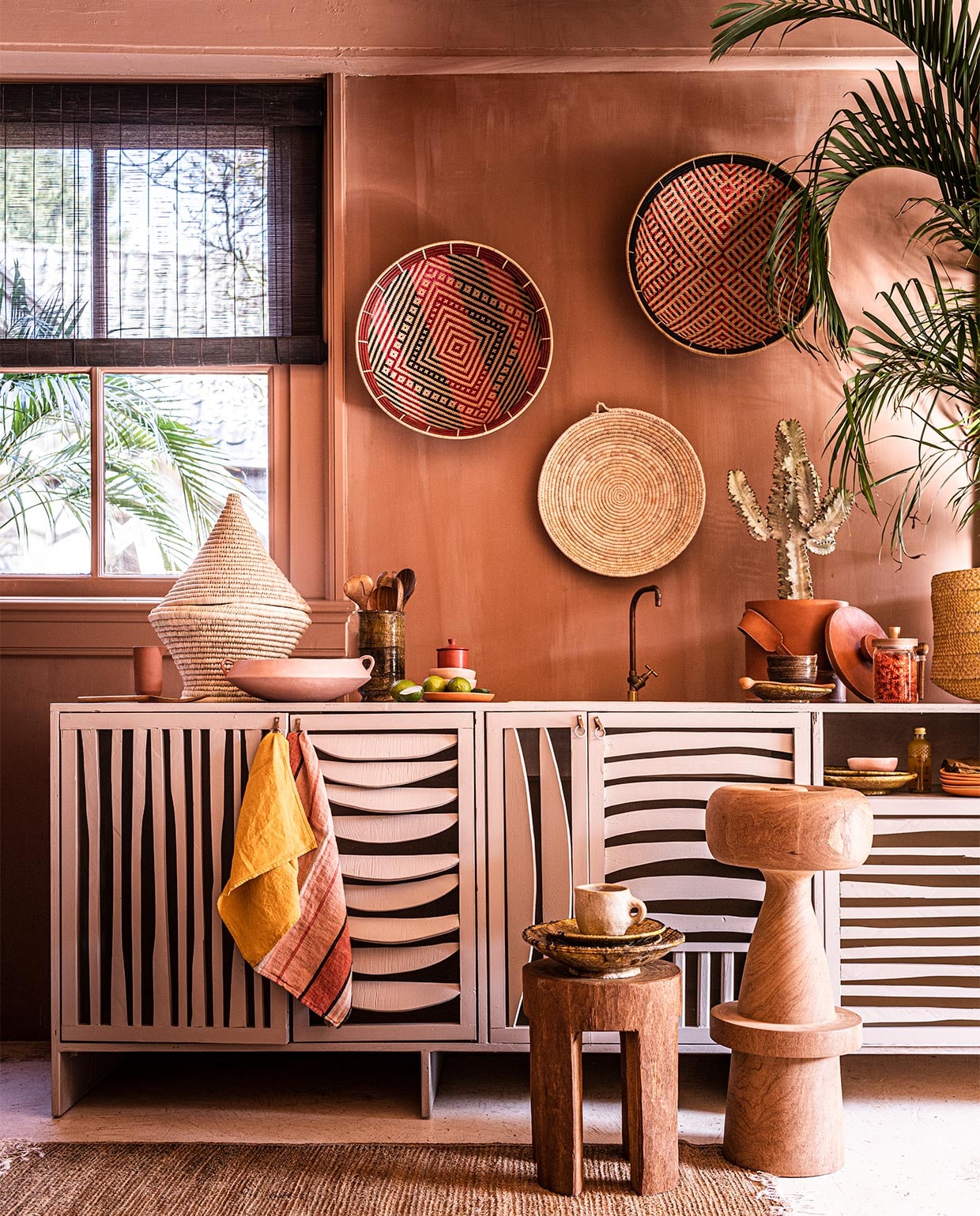 Verfkleur op de wand Cypria van Carte Colori, 2,5 liter, leren wijn- koeler (brechtmurreatelier.nl). Handgemaakte keuken inclusief kraan, (com-anders.nl). Gekleurde manden aan muur, per stuk, effen blanke mand aan wand, vloerkleed, 150×78 cm, geel linnen servet, 45×45 cm, beige kan, gele mand, mand met deksel, bruin servet, 45×45 cm (couleurlocale.eu). Houten lepels (koconceptstore.nl). Planten en cactus (plantje.nl). Grote roze schaal, oranje borden, roze bakjes, flesje met gele limonade (sissy-boy.com). Houten barkruk, lage kruk (polspotten.nl). Groene borden, groene vaas (householdhardware.nl). Rood potje met deksel, linnen theedoek met strepen (maisonnl.com). Bruin flesje, bruine bakjes klein, (letoile.store). Glazen pot (zarahome.com). vtwonen 07-2021 | styling Liza Wassenaar | fotografie Sjoerd Eickmans