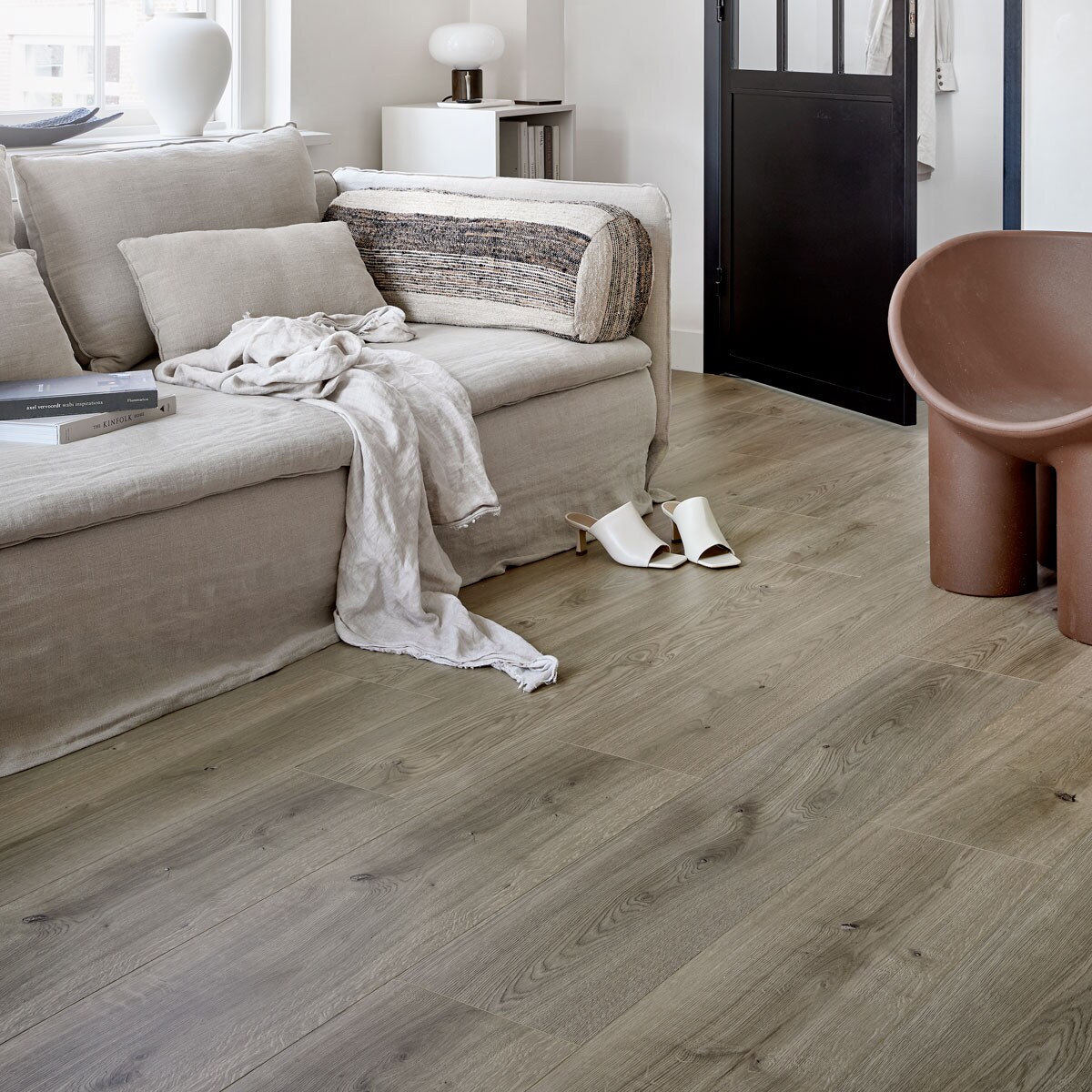 EVC vloer Oat per m² € 39,99. M.m.v. karwei.nl (op maat gemaakt lichtdoorlatend plisségordijn in kleur Linnenbeige A 18074), ikea.nl (bank Söderhamn), bemz.com (linnen bankhoes), zarahome.com (linnen plaid, zwarte schalen, witte vaas), stories.com (schoenen), puurdesign.nu (bruine stoel Roly Poly van Driade), casagitane.com (rond kussen Tronc), newworks.dk (tafellamp), bauwerkcolour.com (muurverf in kleur Mykonos). Overig privébezit. vtwonen 08-2021 | productie Tanja Saarberg | styling Kim van Rossenberg | fotografie Peggy Janssen