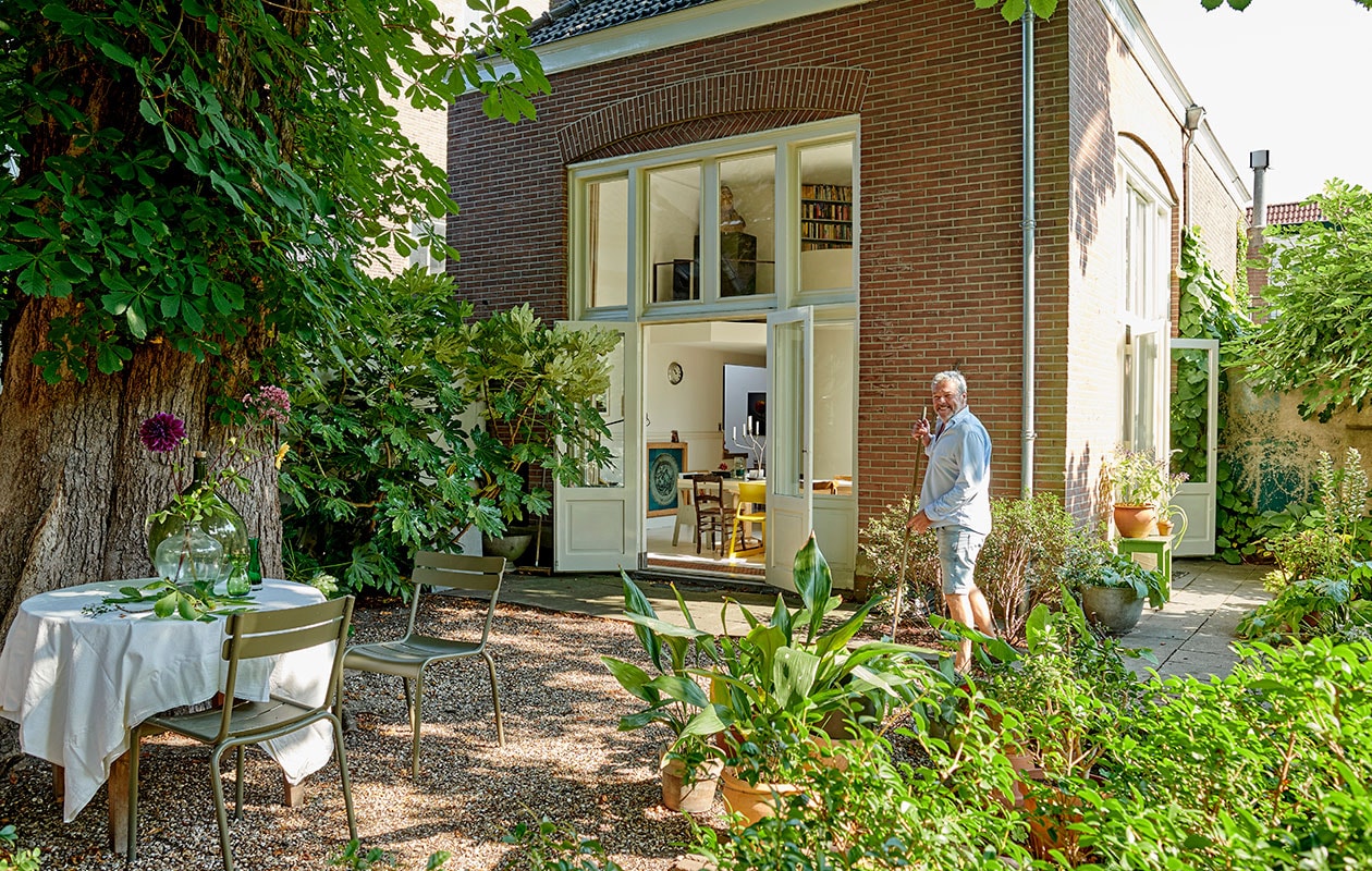 Ronde houten tafel tweedehands. Linnen tafelkleed MrsBloom. Stoelen Luxembourg van Fermob. Plant op de achtergrond: siergember (Hedychium gardnerianum), op de voorgrond Ficus Brown Turkey. vtwonen 07-2021 | productie Features &amp; More | styling Wilma Clusters | fotografie Renee Frinking \ntekst Chantal Hintze | tekstbewerking Laura Zuidema