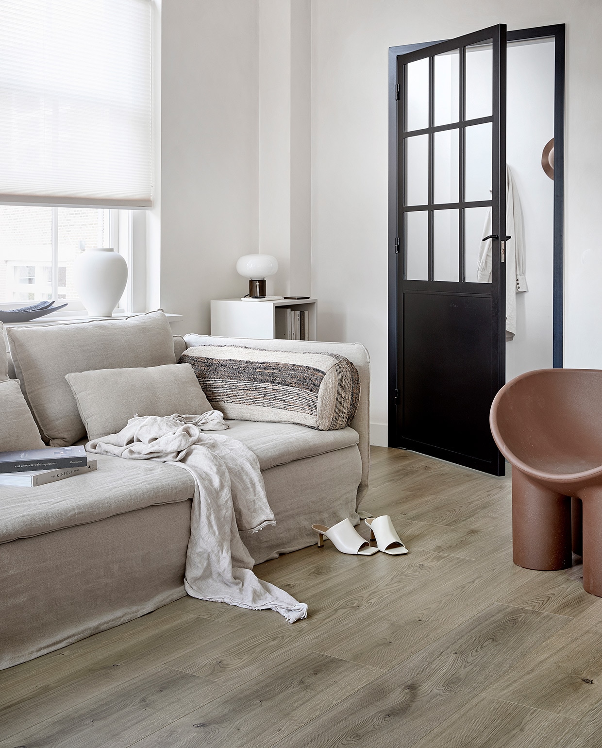 EVC vloer Oat. M.m.v. karwei.nl (op maat gemaakt lichtdoorlatend plisségordijn in kleur Linnenbeige A 18074), ikea.nl (bank Söderhamn), bemz.com (linnen bankhoes), zarahome.com (linnen plaid, zwarte schalen, witte vaas), stories.com (schoenen), puurdesign.nu (bruine stoel Roly Poly van Driade), casagitane.com (rond kussen Tronc), newworks.dk (tafellamp), bauwerkcolour.com (muurverf in kleur Mykonos). Overig privébezit. vtwonen 08-2021 | productie Tanja Saarberg | styling Kim van Rossenberg | fotografie Peggy Janssen