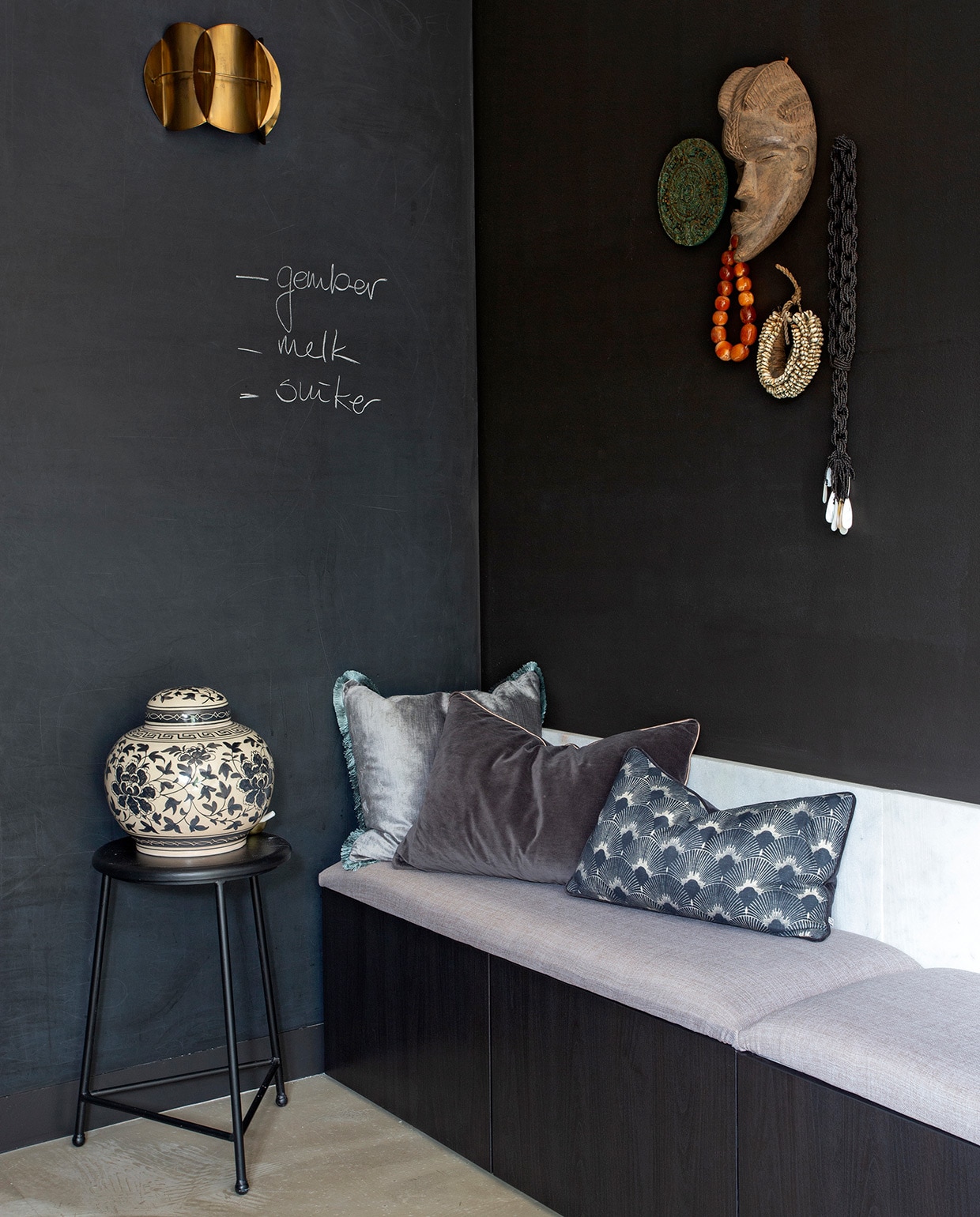 Muurverf Raaf Histor. Bank van Bestå element Ikea. Zitkussens zelfgemaakt. Kussen blauwgrijs en antraciet H&amp;M Home. Kussen met waaier House Doctor. Vaas met deksel Ibiza Outdoor. Wandlamp HomeStock. Zwarte kruk, decoratiebord, masker, schelpenketting, zwart-witte kralenketting kringloopwinkel. vtwonen 06-2021 | styling Liesbeth Visschedijk | fotografie Jeltje Janmaat | tekst Adeline Mans