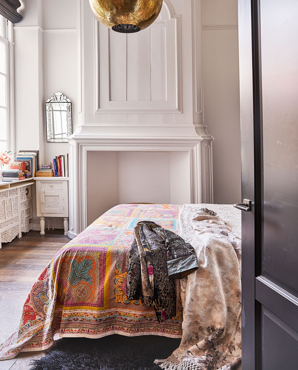 Kleurig tafelkleed van Zara Home als sprei op bed. Kimono zelfgemaakt, sprei van gemarmerd katoen uit India. Lamp en kastje, waar Karin zelf nog poten onder zette, Zenza. Venetiaanse spiegel van een rommelmarkt. Schouw origineel. Radiatorombouw zelfgemaakt met een Indiaas kamerscherm. vtwonen 06-2021 | productie Coco Features | styling Linda van der Ham | fotografie Peggy Janssen