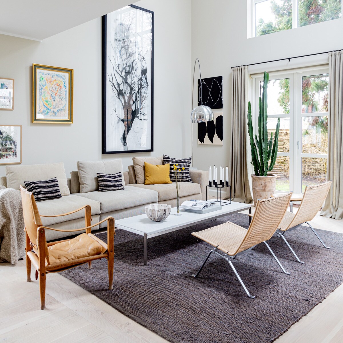 Muurverf Shaded White vanFarrow &amp; Ball. Bank Eilersen. KussensTapet-Cafe. Koffietafel PK62 en rotanstoelen PK22 van Poul Kjærholm voorFritz Hansen. Leren stoel Kaare Klintvoor Carl Hansen &amp; Son. VloerlampArco van Flos. Schaal gemaakt dooreen vriendin. KaarsenstandaardMogens Lassen. Schilderijen van linksnaar rechts Carsten Dahl (twee maal),Eigill Jacobsen, Cathrine RabenDavidsen. Grafische kunstwerkenUlla Pedersen. Vloerkleed Tine K Home. vtwonen 13-2020 | Productie Living Inside | Styling Henrietta Sharma | Fotografie Annita Behrendt | Tekst Adeline mans, Pia Olsen
