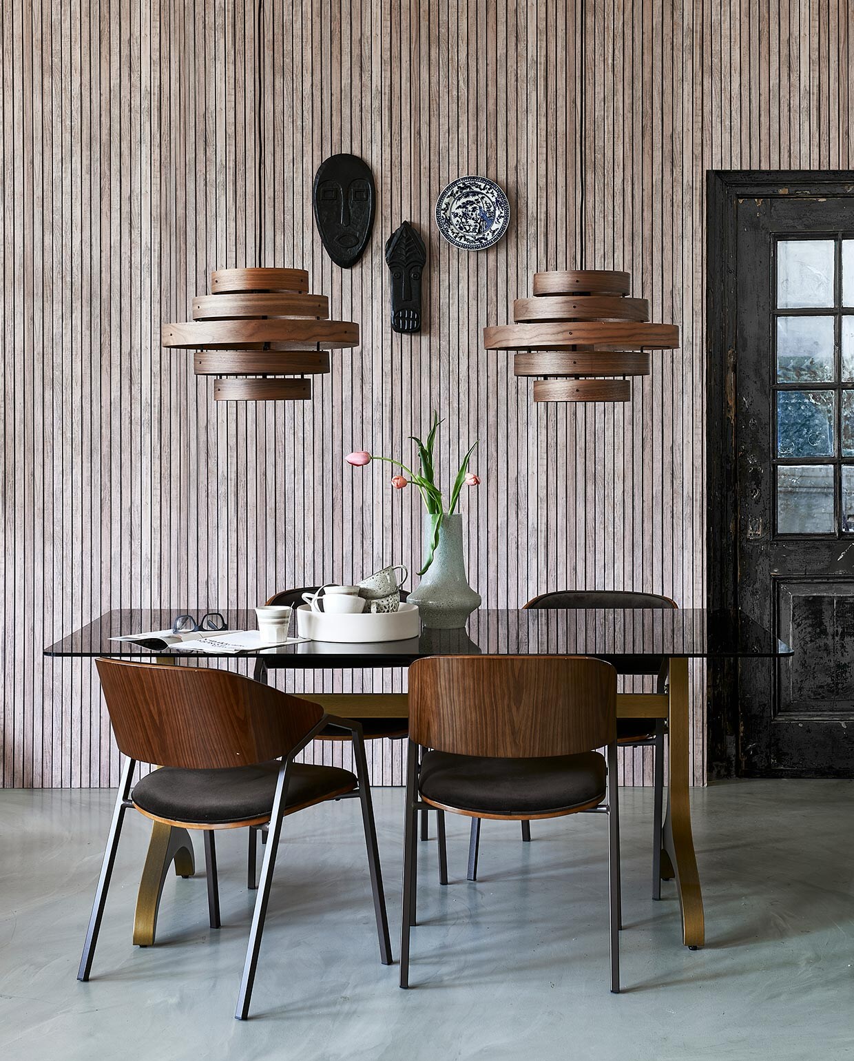 Vliesbehang met lattenprint van vtwonen (karwei.nl). Glazen tafel Sansa met messing onderstel, 180x90x75 cm (lxbxh) (dutchbone.com). StoelenClan, maskers Xara en Xavi, vaas (basiclabel.nl). Bord aan wand Kyoto, mok met streep(hkliving.nl). Walnoothouten hanglampen van Eth, 50 cm (Ø) (vtwonen.nl). Witte schaal Dixon op tafel, 32,8×7,8 cm (Øxh) (festamsterdam.com). Mokken in schaal (hm.com). vtwonen 06-2021 | styling Fietje Bruijn | fotografie Dennis Brandsma
