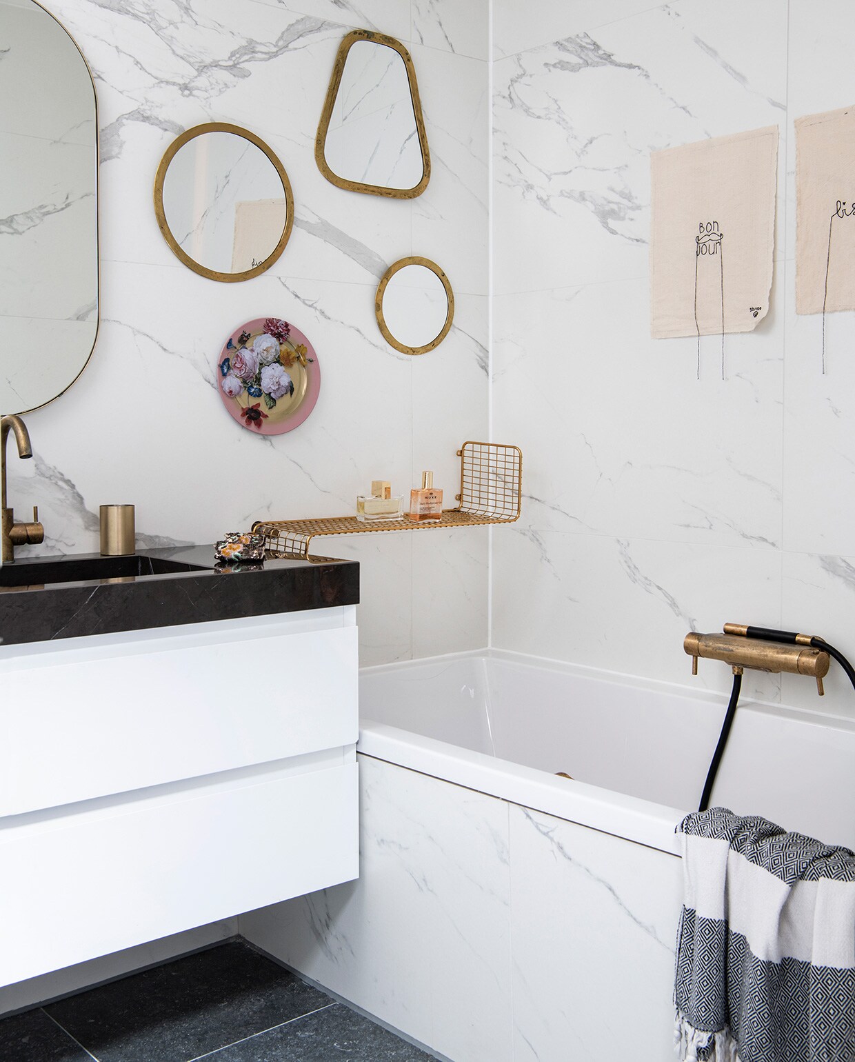 Badkamer en tegels via Ton Scholten Tegelhandel, kranen van Hotbath, messing beker uit India, grote spiegel van Made. Wandspiegels van Household Hardware, roze gebloemd bord van Loods 5, messing rek van Ikea. Hammamdoek over badrand van El Ramla Hamra. Kunstwerkjes met stikwerk boven het bad van Lemonwise. vtwonen 06-2021 | productie Insidehomepage | styling Inge van Lieshout | fotografie Louis Lemaire