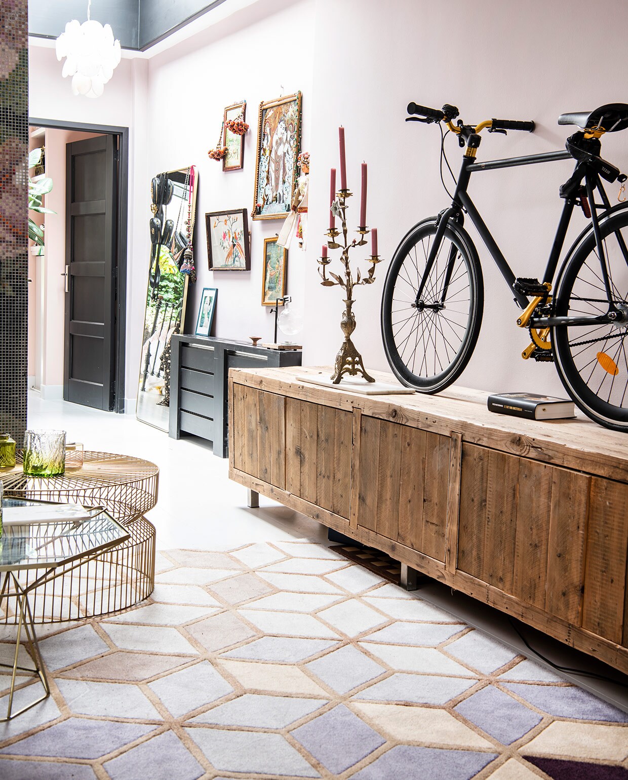 Op de wand krijtverf van Dubbelleven in de kleur Zoet. Houten dressoir van Leeelijk, fiets van Made, net als de spiegel links. Vijfarmige (antieke) kandelaar uit Puglia. Witte hanglamp van Zenza. Geborduurd schilderij van de Noordermarkt, andere schilderijen privébezit, prenten en handgemaakte kettingen uit India, antieke Chinese pop uit Parijs. Kleed van Rozenkelim. Tafel met glazen blad van L’Etoile, salontafel van draadstaal van Zara Home. vtwonen 06-2021 | productie Insidehomepage | styling Inge van Lieshout | fotografie Louis Lemaire