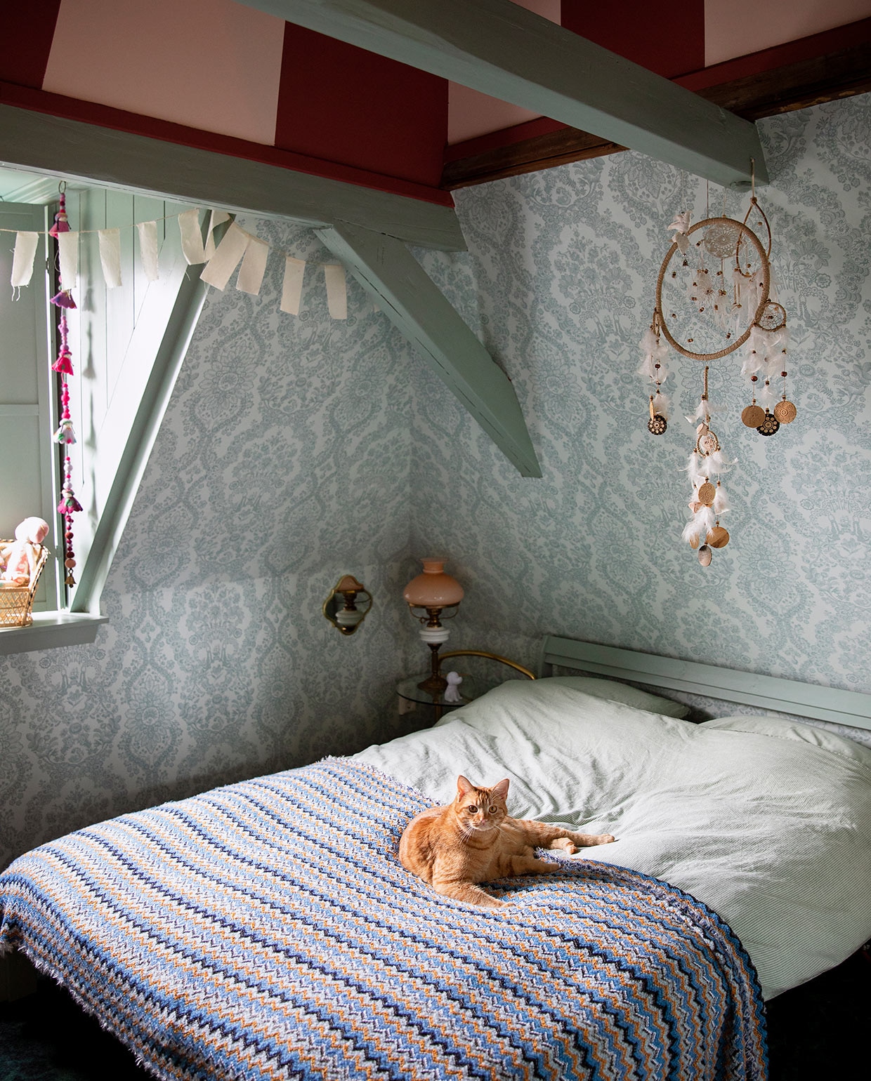 Verfkleur strepenprint Blossom en Dining Room Red, houtwerk Aloë Vera van Painting The Past. Behang Lacy Dutch van Pip Studio. Slinger Sukha. Wandspiegel H&amp;M. Nachtkastje Ouderwets Gezellig. Lamp kringloopwinkel. Bed Neiden en beddengoed Ikea. Dromenvanger wereldwinkel. Kwastjeskoord en sprei herkomst onbekend. vtwonen 06-2021 | styling Ilona Jongepier | fotografie Dana van Leeuwen