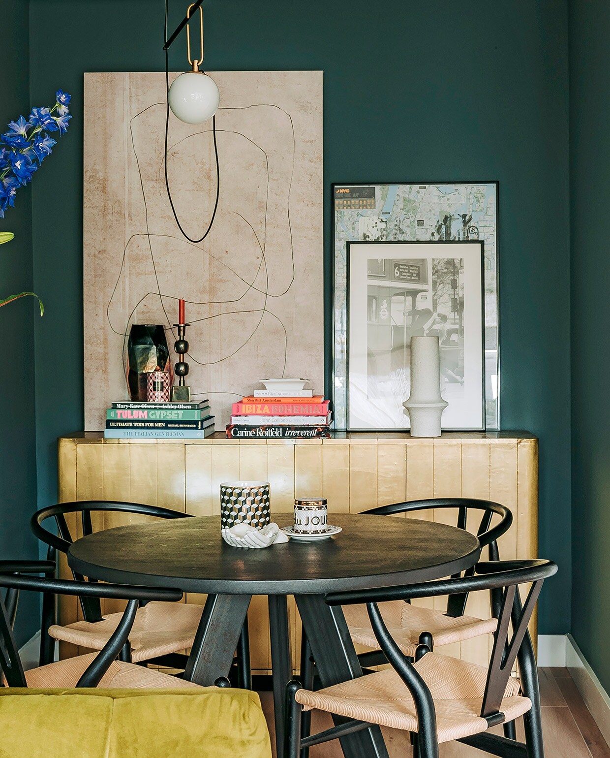 Hoge vaas Menu, bronzen bijzettafel Rapture Interior Luxury, spiegel HKliving. Muurverf Inchyra Blue van Farrow &amp; Ball. Tafel Marktplaats, stoelen Sklum, kop-en-schotel Anthropologie, wit schaaltje en zwart-wit vaasje H&amp;M Home. Dressoir Loods 5, boeken via Nox Studio Interiors en Assouline. Kandelaar, vaas en witte vaas Nox Studio Interiors. Geurkaars H&amp;M Home, schilderij en schaaltje Zara Home. Zwart-witte foto in lijst van Annes moeder geweest, lijst met poster gekocht op straat in New York. Hanglamp Artemide. vtwonen 06-2021 | Productie CocoFeatures | Fotografie Muk van Lil | tekst Cathelijne van Wingerden