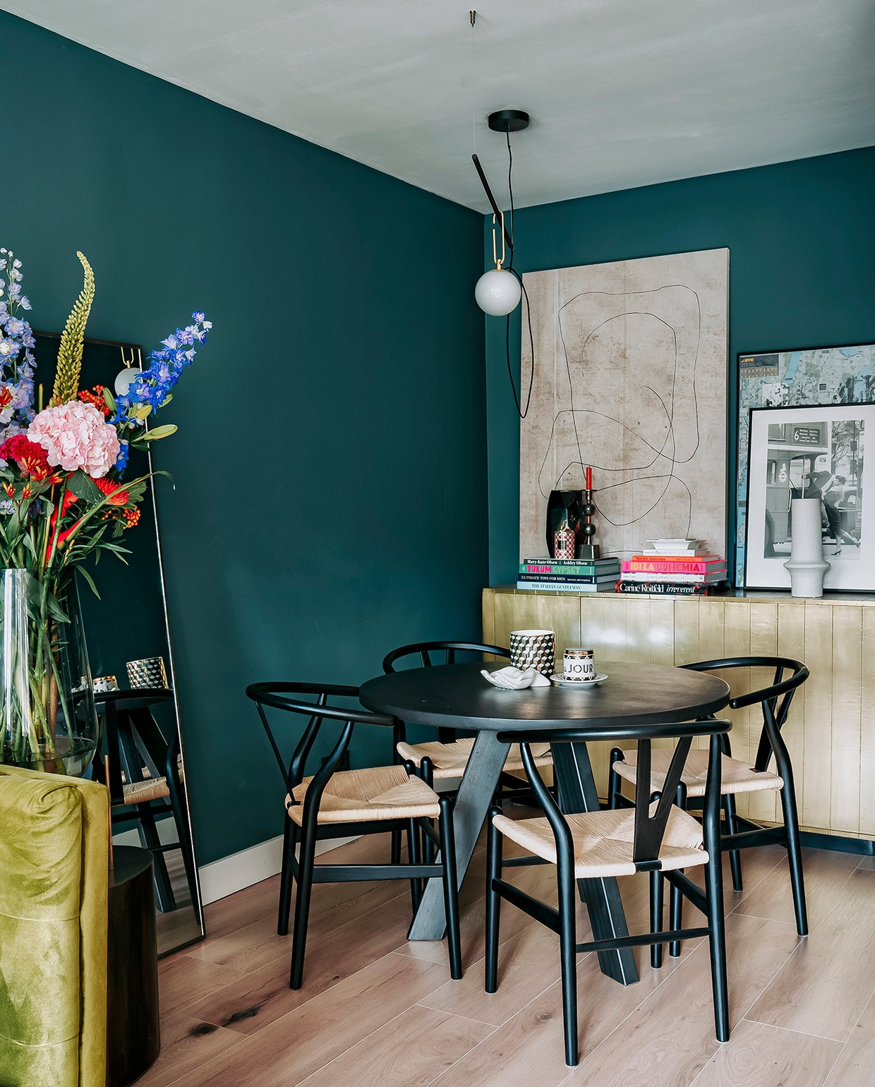 Hoge vaas Menu, bronzen bijzettafel Rapture Interior Luxury, spiegel HKliving. Muurverf Inchyra Blue van Farrow &amp; Ball. Tafel Marktplaats, stoelen Sklum, kop-en-schotel Anthropologie, wit schaaltje en zwart-wit vaasje H&amp;M Home. Dressoir Loods 5, boeken via Nox Studio Interiors en Assouline. Kandelaar, vaas en witte vaas Nox Studio Interiors. Geurkaars H&amp;M Home, schilderij en schaaltje Zara Home. Zwart-witte foto in lijst van Annes moeder geweest, lijst met poster gekocht op straat in New York. Hanglamp Artemide. vtwonen 06-2021 | Productie CocoFeatures | Fotografie Muk van Lil | tekst Cathelijne van Wingerden