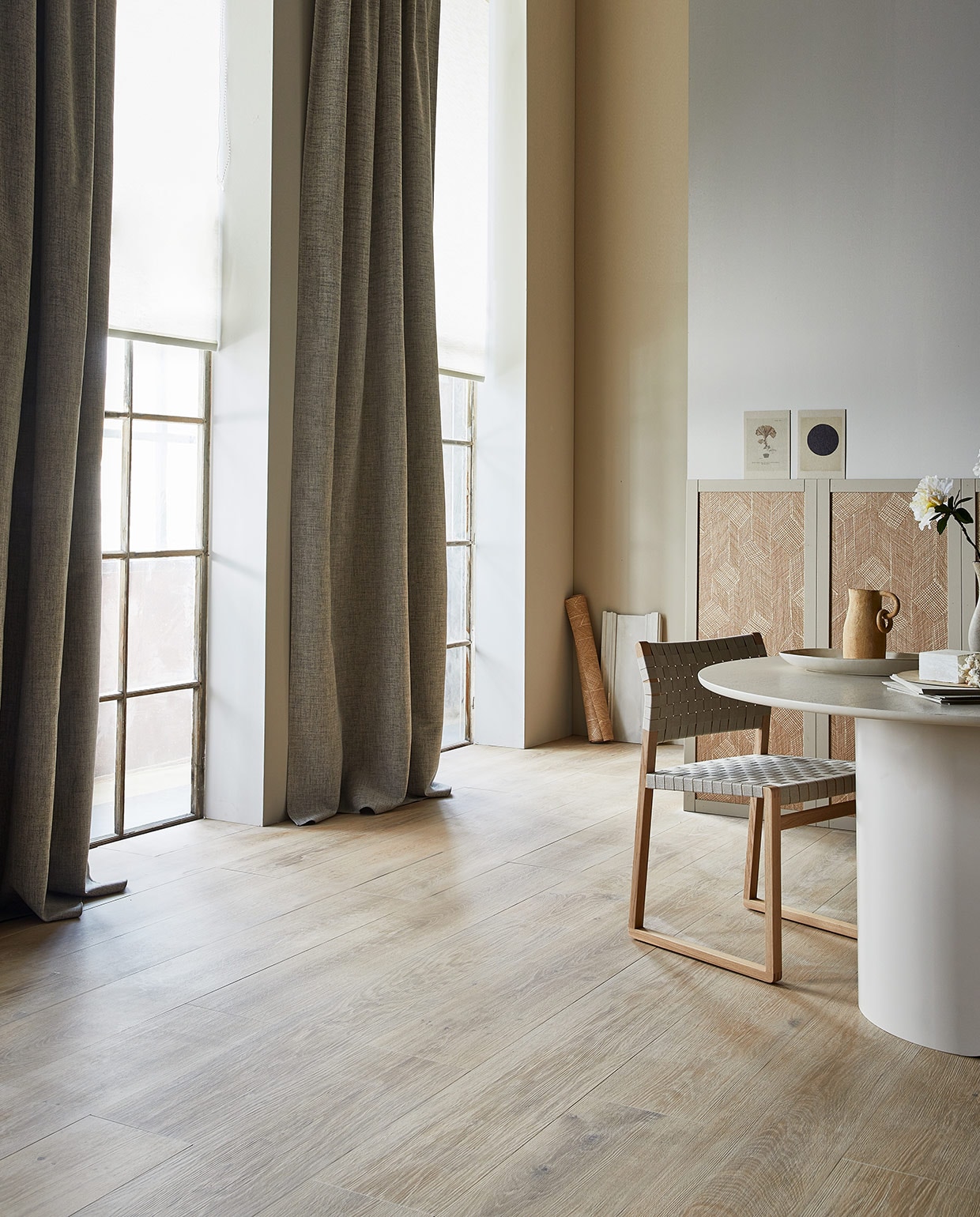 Gordijn Groove, wit-grijs verduisterend, met plooi, 270×140 cm (hxb). Rolgordijn Dawn, off-white, lichtdoorlatend, 190×60/90/120/150/180/210 cm (hxb). M.m.v. vtwonen.nl (vloertegels Composite Multicolor van vtwonen), karwei.nl (muurverf Flax van vtwonen), designtales.nl (stoel van Fredericia), festamsterdam.com (eettafel Plateau), studio-yen.com (kan), arte-international.com (behang Shibam uit de collectie Cameo), hm.com (schaal). Overig privébezit. vtwonen 07-2021  | Productie Tanja Saarberg | Styling Cleo Scheulderman | Fotografie Jeroen van der Spek\n\nvtwonen 07-2021 | licht huis met grijze gordijnen, een witte ronde tafel, en landhuiseffect
