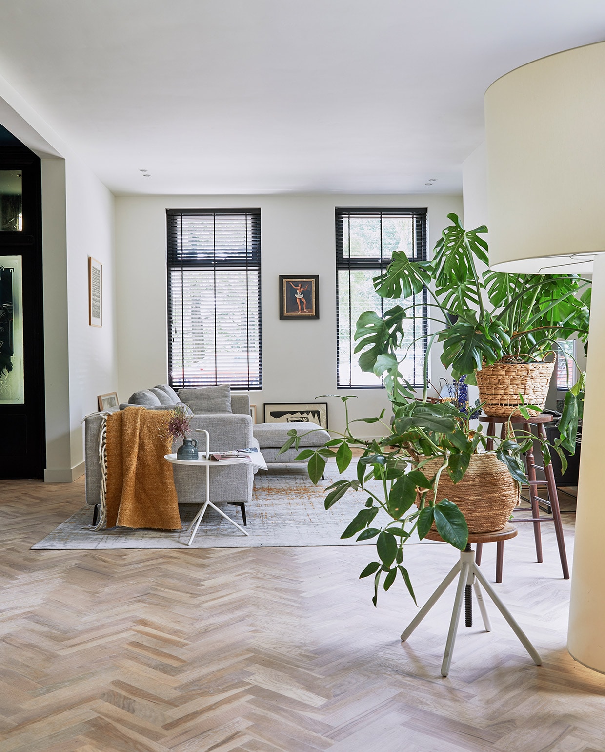 Bank Zitmaxx Wonen, vloerkleed Louis de Poortere, bijzettafel Hay, plaid Kwantum. Lage kruk Marktplaats, hoge kruk uit de inboedel van het huis. Rieten plantenmanden Xenos, schilderij op de grond Wally Elenbaas, schilderij van ballerina Herman Bieling, witte staande lamp Big Shadow van Cappellini. vtwonen 05-2021 | fotografie Peggy Janssen | tekst Cathelijne van Wingerden