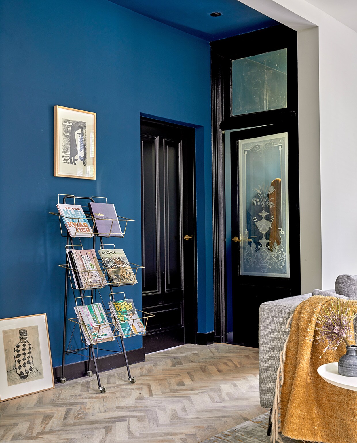 Eikenhouten visgraatvloer Balkan Wood, muurverf Haags Blauw van Farrow &amp; Ball, tijdschriftenrek kringloopwinkel, schilderij aan de muur Wally Elenbaas, schilderij op de grond Jaap Kraanen, plaid Kwantum. Verf deuren en plinten grafietzwart Ral 9011. vtwonen 05-2021 | fotografie Peggy Janssen | tekst Cathelijne van Wingerden
