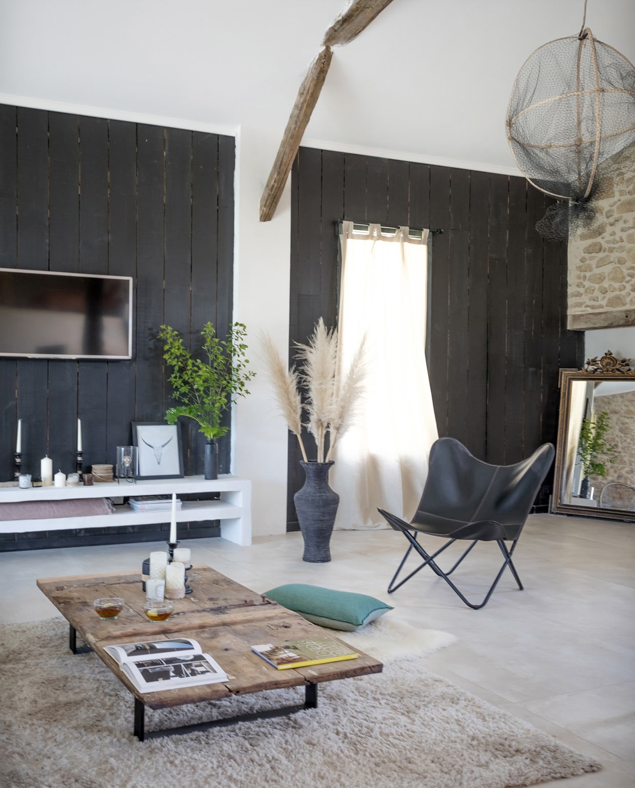 Vloerkleed en bank Castorama, vlinderstoel van een Franse Marktplaats. Plaid en kussens Maison de Vacances. Zwarte vazen via Etsy, gordijnen La Redoute, lijst Desenio. Visnetten zelfgemaakt, salon- tafel zelfgemaakt van een , oude deur. Overig herkomst onbekend. vtwonen 05-2021 | productie AC Scoffoni | fotografie Cécile Perrinet-Lhermitte | styling Marie-Maud LevRon