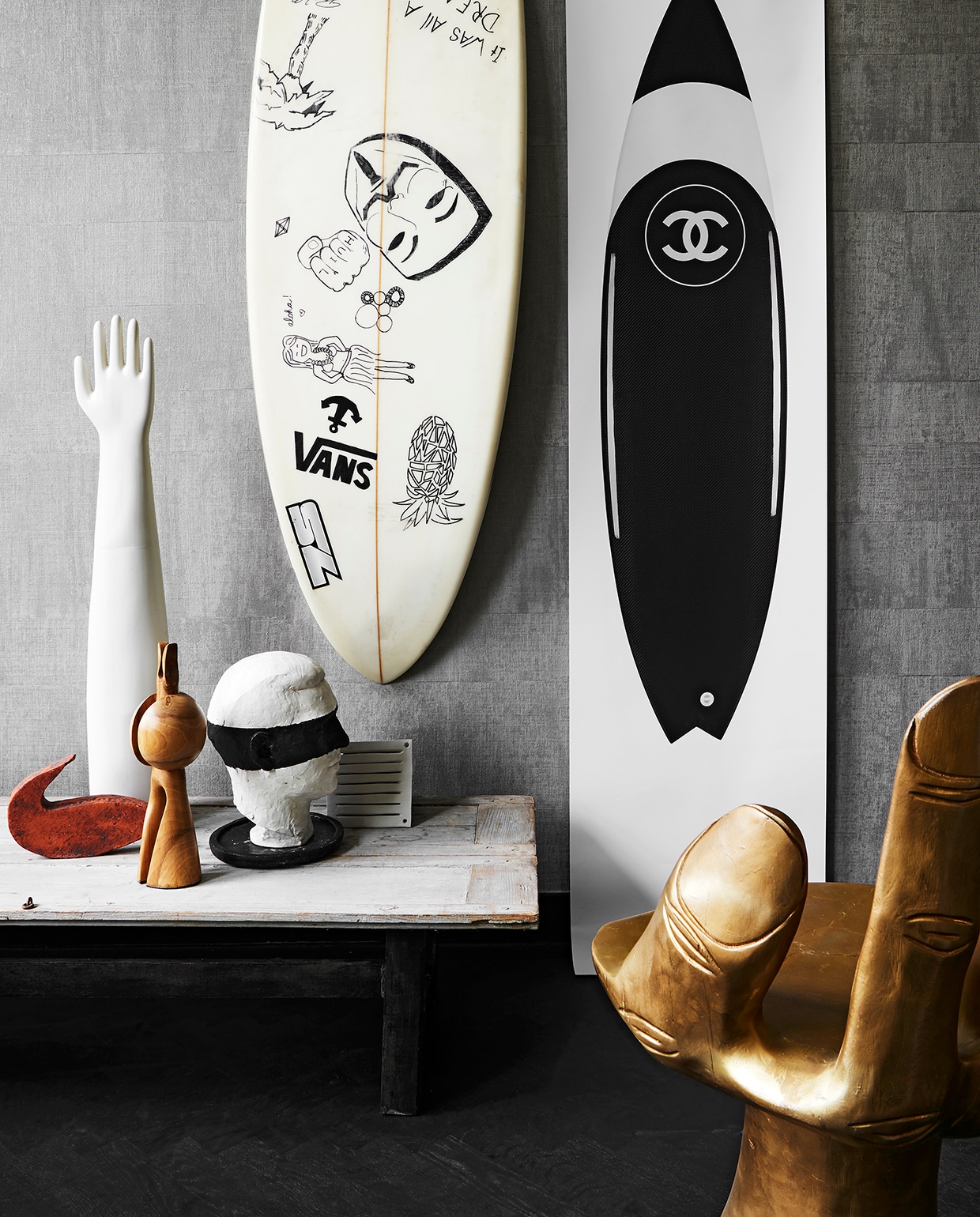 Foto Chanel-surfplank geprint op rol behangpapier (copyshop). Vintage surfplank witte kop met geschilderd masker, notenhouten object Pion No 45 van C. v.d. Meijden (nrdrhvn91.nl). Vintage houten stoel in de vorm van een hand, goud gespoten houten (polspotten.nl). Terracotta vis, handschoenmodel van wit keramiek van Sip &amp; Clara (itfinkeboskje.nl). Rooster van keramiek (printlove.nl). Overig privébezit.
