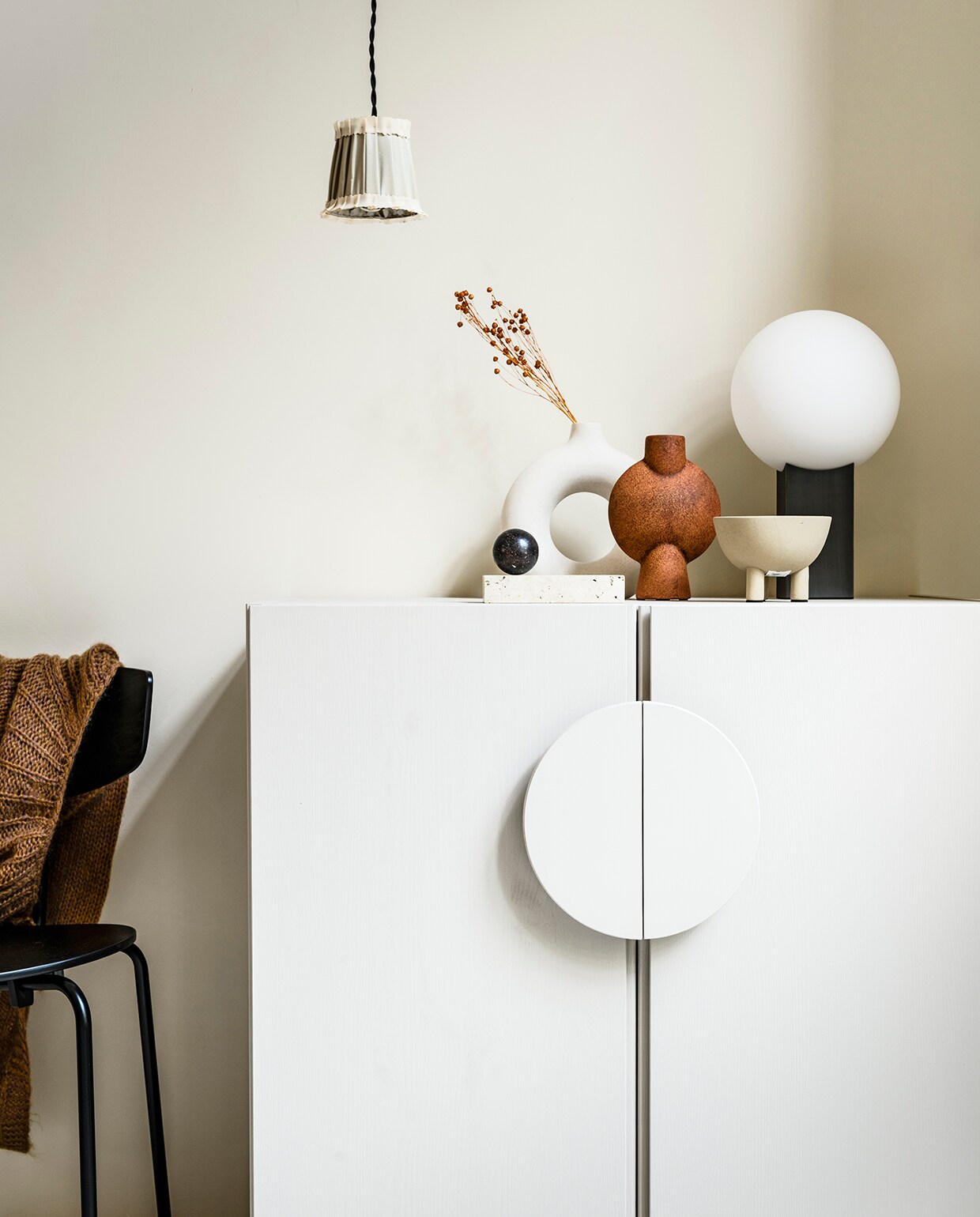 Stoel Herman van Ferm Living (vtwonen.nl), gebreid vest (fishonthemoon.com). Hanglamp La Balladeuse van Vox Populi (maisonnl.com). Keramieken vaas met gat (hm.com). Stenen blok Travertine (thefinestore.com), marmeren bal (privébezit). Vaas Sphere Vase Bubl in kleur terracotta, 18x14x5,5 cm (hxbxd), schaal op pootjes Duck Bowl in kleur sand, 12×9,5 cm (Øxh), tafellamp Hoop, 20×34 cm (Øxh) (101cph.com). Muur geverfd in kleur mikonos van We Are Wow Makers p.o.a. (anoukb.com).