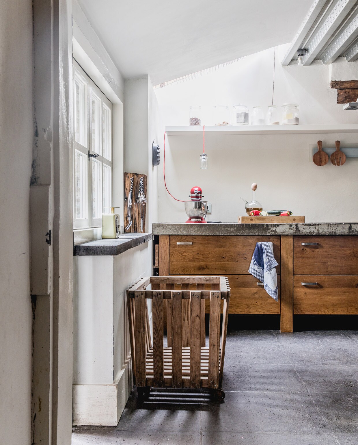 Betontegelvloer Schellevis ingewreven met Oxan olie. Keuken ontworpen en gemaakt door Jan en zoon Ruben. Oude wasmand afkomstig uit een hotel. Keukenmachine KitchenAid. Weegschaal Emmaus. Bestekrek zelfgemaakt van oude spoorbiels. Bestek meegenomen uit Frankrijk. Hanglamp zelfgemaakt van jampot en rood snoer van Snoerboer. Houten lepel en vork cadeau gekregen. Vintage oliekan uit Spanje. Overig herkomst onbekend. vtwonen 05-2021 | productie Features &amp; More | styling Wilma Custers | Fotografie Ivar Janssen