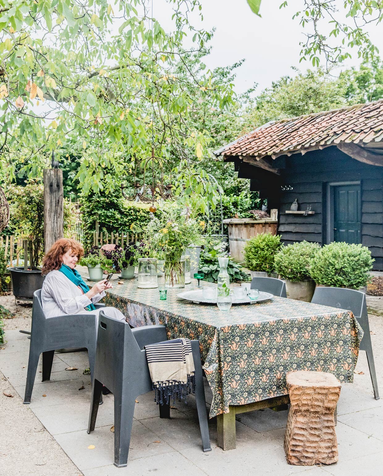 Houten buitentafel gemaakt door Jan. Weerbestendig tafelkleed William Morris. Tuinstoelen Leen Bakker. Pilaar Emmaus. Overig herkomst onbekend. vtwonen 05-2021 | productie Features &amp; More | styling Wilma Custers | Fotografie Ivar Janssen