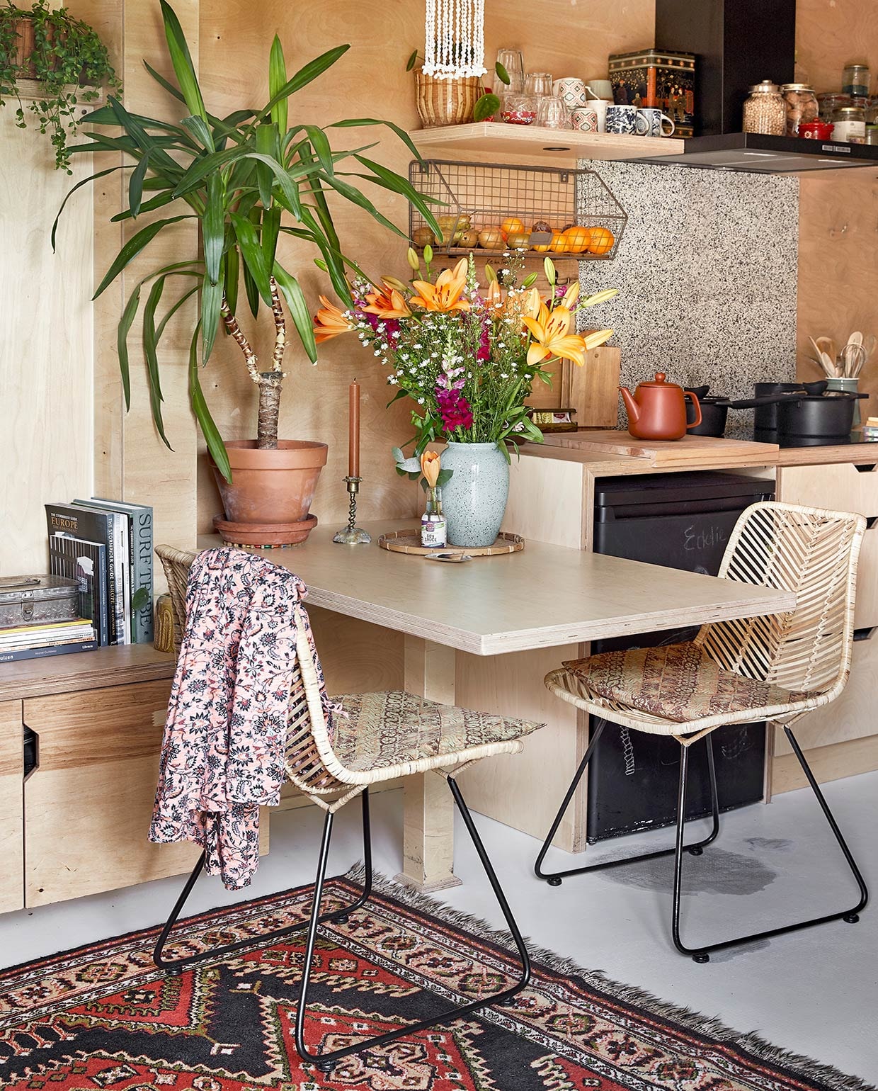 Vloerkleed van Carmens ouders geweest. Lage inbouwkast en eettafel zelfgemaakt. Stoelen Van Til Outlet. Onderzetter souvenir uit Indonesië. Flesjes en fruitmand Kitchen Trend. Glazen Duralex. Mokken Tastoe en kringloop. Voorraadpotten Clayre &amp; Eef. Hanglamp Curms. Theepot Xenos. Gietijzeren pannen en kookplaat herkomst onbekend. Achterwand kookplaat restpartij tegels gekregen van de buren. Keukengereihouder Dille &amp; Kamille. Vloer egaline gietvloer met Eurocol-coating. vtwonen binnenkijken special tiny houses | styling Iris van der Meer | fotografie Peggy Janssen | tekst Cathelijne van Wingerden