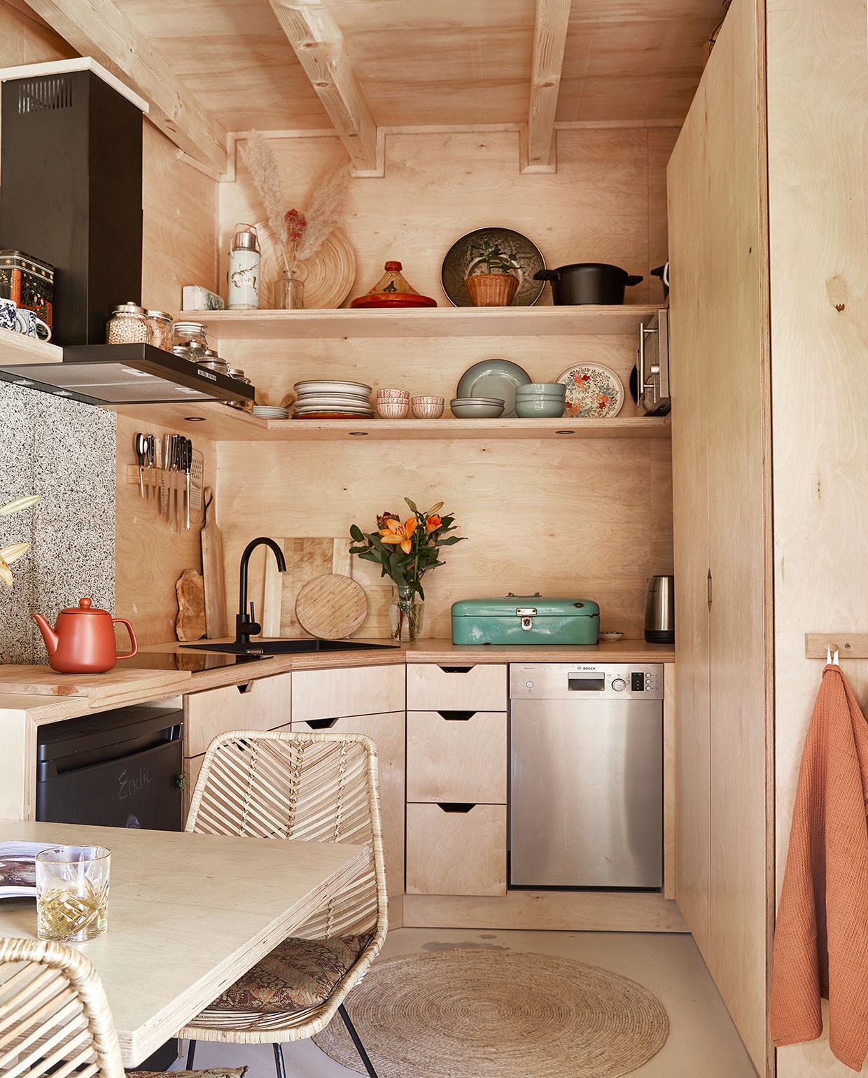 Eettafel zelfgemaakt. Stoelen Van Til Outlet. Koelkast tweedehands, zwart geverfd met krijtbordverf. Theepot Xenos. Kraan Praxis. Messen, scharen, houten snijplanken herkomst onbekend. Bamboe messenhouder Duikelman. Groene broodtrommel van Carmens ouders geweest. Potten op afzuigkap Clayre &amp; Eef. Servies op de planken kringloop, rommelmarkt en van Carmens oma geweest. Thermoskan en gebloemd bord Tastoe. Vaas met droogbloemen, rieten bord, tajine herkomst onbekend. Schaal kringloop. Gietijzeren pan The White Series. Vaatwasmachine Bosch. Theedoek Kwantum. vtwonen binnenkijken special tiny houses | styling Iris van der Meer | fotografie Peggy Janssen