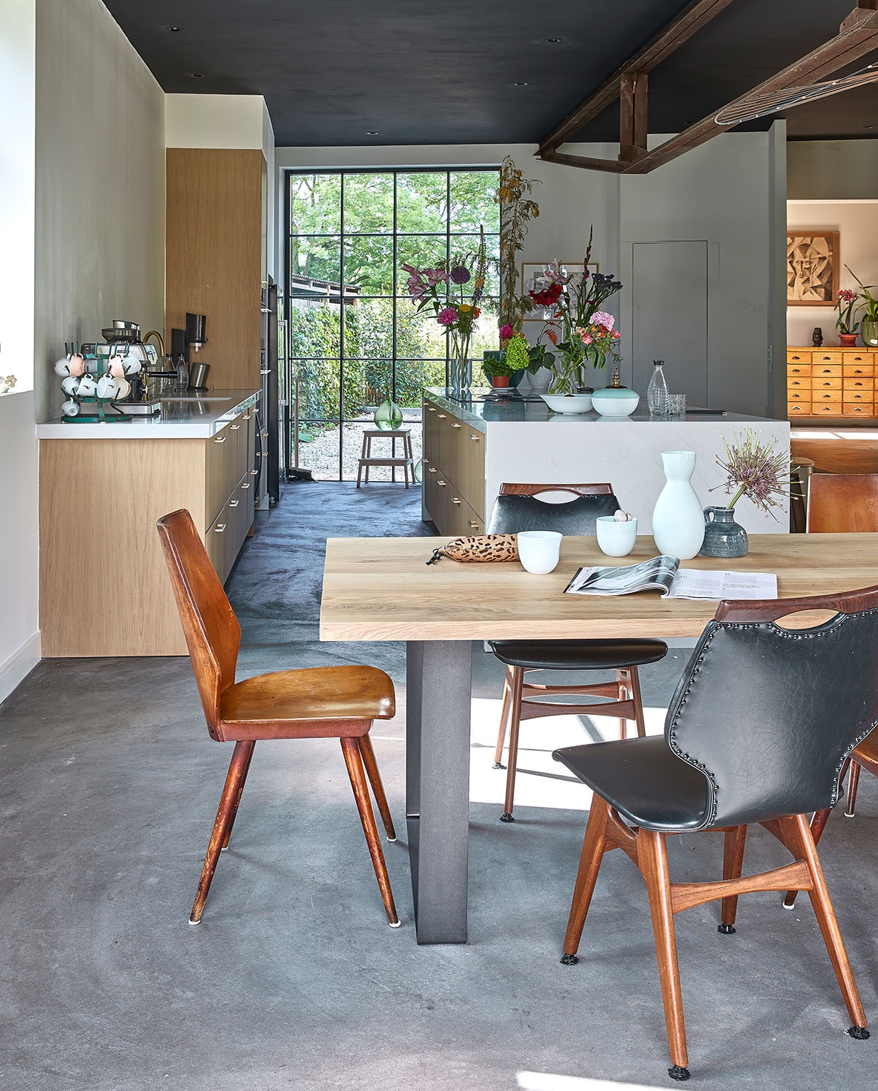 Tafel Houthandel Woerden, stoelen kringloop en brocante. Mokken, witte vaas en witgroene vaas Design Studio Carola Zee. Etui Mango, groene vaas Action. Keuken Ikea, blad Kemie, fronten K14. Schaal en waterkaraf Sodastream, glas en kruk Ikea. Vazen door de jaren heen verzameld, bloemen The Flower Factory. Groene vaas op kruk vintage. Verf plafond grafietzwart Ral 9011. Vloer zandcement. vtwonen 05-2021 | fotografie Peggy Janssen