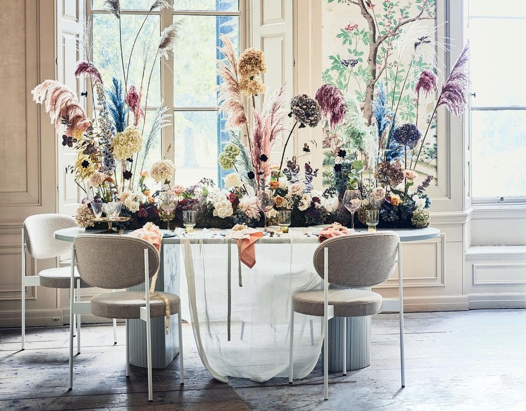 Bloemenloper prijs op aanvraag (edenique.nl). Tafelkleed gemaakt van kaasdoek per meter € 2,- (boerenbonthal.nl). Stoelen van Verpan vanaf € 732,- (dezaakdesign.nl). Ovale tafel, op maat gemaakt, 220x110x76 cm vanaf € 750,- (com-anders.nl). Waterglazen € 7,95, goudkleurig bestek € 49,25, diner­borden € 21,95, mintgroene borden € 14,50 (vtwonen.nl). Servetten € 6,20, roze wijnglazen met goudkleurige rand € 9,65 (nordal.eu). vtwonen jubileum 10-2019 | styling Cleo Scheulderman | fotografie Jeroen van der Spek