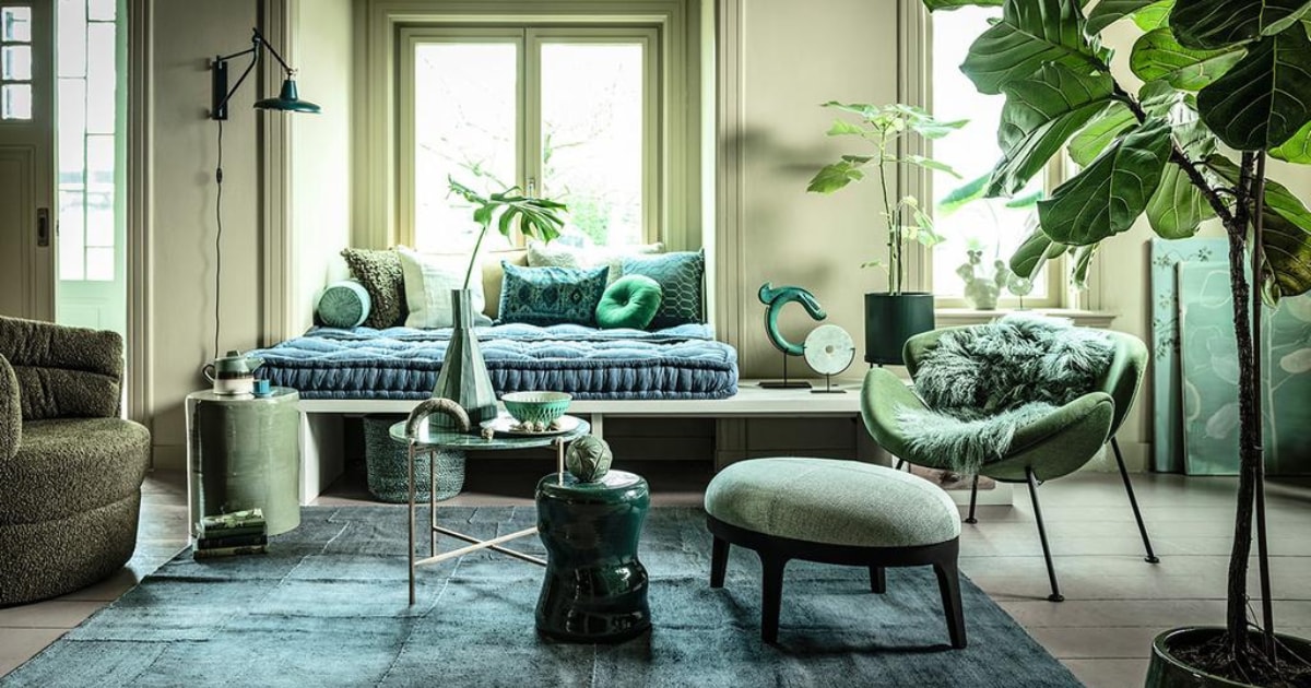 Fauteuil links € 795,- (flinders.nl). Bank op maat gemaakt, prijs op aanvraag (com-anders.nl). Zitting bank twee stuks op maat gemaakt, 210×80 cm € 690,-, geel/groen langwerpig kussen € 154,- (coco-mat.com). Fauteuil Orange Slice van Artifort € 1972,-, cactus van Hay € 75,- (homestede.nl). Marmeren tafel € 95,-, kruk links € 195,-, kruk midden € 103,95, kussen langwerpig met oude opdruk € 69,-, ronde sierbol op kruk prijs op aanvraag, sierobject draak € 129,95, vacht € 99,-, (loods5.nl). Poef € 1150,-, grof kussen € 105,-, kussen geometrisch € 108,- (covanderhorst.nl). Marmeren sierobject op tafel € 49,95 (wonenmetlef.nl). Bord, per 6 € 89,95 (livingandcompany.com). Theepot € 29,95 (bijenkorf.nl). Vloerkleed, 242×178 cm € 1195,-, langwerpig kussen achter € 275,-, lichtgroen kussen voor € 49,-, mand € 39,-(couleurlocale.eu). Wandlamp Hector van Dutchbone € 149,-, rond kussen Mandarin van Kaat Amsterdam, Ø 40 cm € 25,50 (vtwonen.nl). Notitieboeken, per stuk € 19,95 (maisonnl.com). Espressokop € 39,50 en schotel € 29,95, schaal € 112,50 (ottomania.nl). Rolkussen € 49,95 (hinck.nl). Hoge vaas € 445,-, ronde siervorm op bank € 120,- en in vensterbank € 69,- (badenbaden.nl). Schilderijen achter Branch on a green canvas, 80×100 cm € 850,- en Floral sketch, original painting, 70×80 cm prijs op aanvraag (maartjevandennoort.nl). Plantenpot op pootjes € 65,- (fermliving.com). Plantenpot op grond € 35,- (uncwardrobe.com). JA | vtwonen 04-2020 | styling Liza Wassenaar | fotografie Sjoerd Eickmans