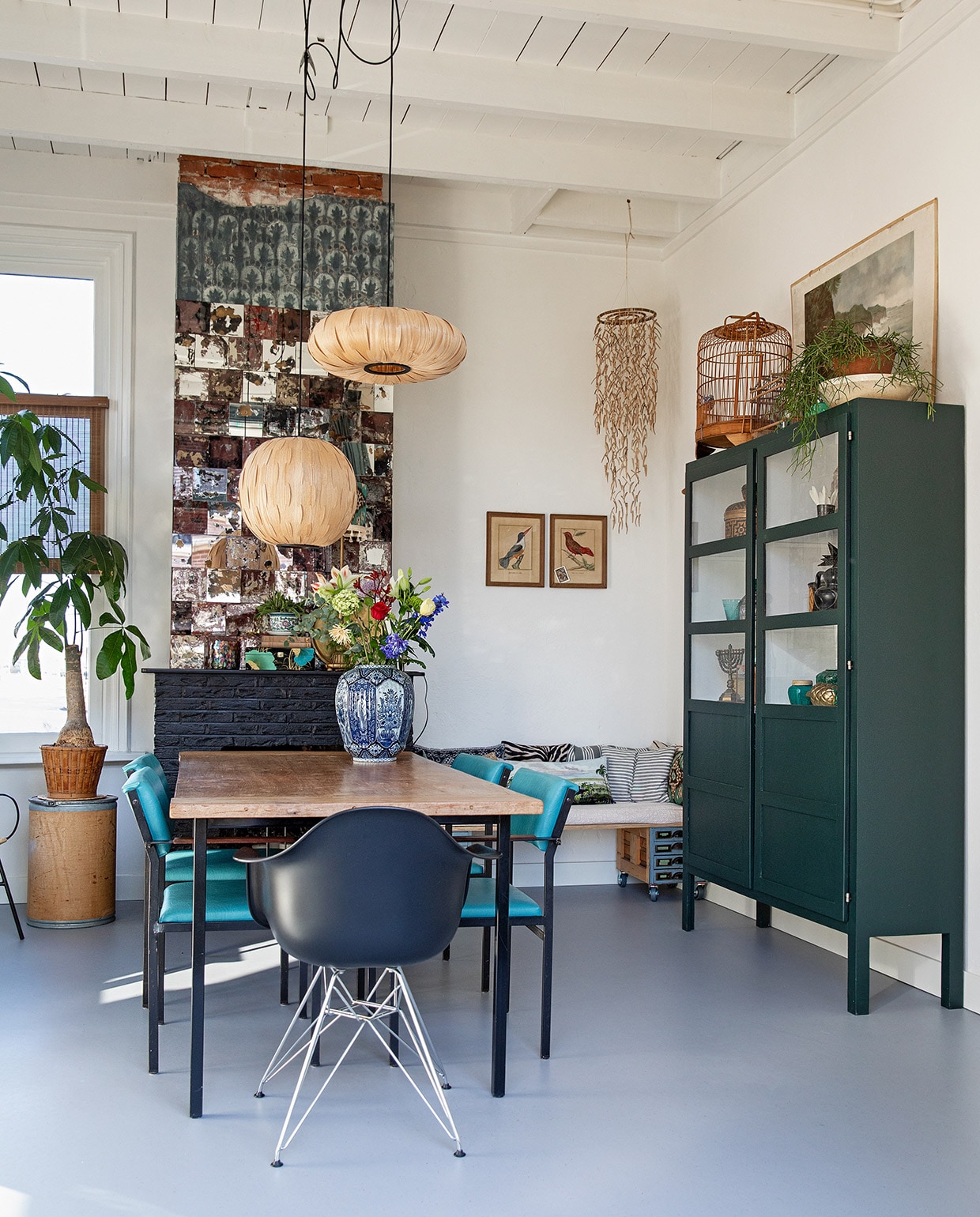 Vloer Marmoleum Cacao in Earl Grey Chocolate via Woontheater de Eclips, ronde kartonnen ton, rieten mand, hangend voorwerp in hoek en etsen aan wand via Bij Lokaal, teakhouten tafelblad vintage met onderstel via Datas, blauwe stoelen Cees Braakman voor Pastoe, zwarte kuipstoel Vitra, hanglampen Dutchbone, Delfts blauwe vaas rommelmarkt, bankje gemaakt van twee vintage archiefkastjes en underlayment, kussens op bank: zebra, verticale streep en horizontale streep gemaakt met vintage stof, landschap Bij Lokaal. Kast zelfontworpen. Op kast: kooi kringloop, witte schaal uit Tsjechië, pot uit Polen, prent achter kast kringloop. vtwonen 04-2021 | styling Ilona Jongepier | fotografie Dana van Leeuwen