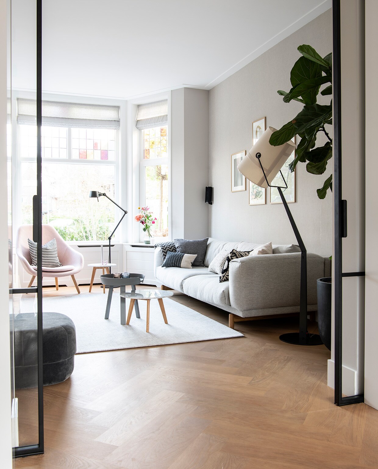 Vloer eiken. Glas in lood gemaakt in Polen. Gordijnen, wit kussen en donkergrijs kussen By Mölle. Bank en grijze bijzettafel Muuto. Plaid Elvang Denmark. Roze fauteuil Hay, gestreept kussen House Doctor. Zwarte vloerlamp Bolt van Tonone. Vloerkleed Limited Edition. Witte bijzettafel Zuiver. Poef Circus van Normann Copenhagen. Rechthoekig kussen en kussen zwart-wit patroon Mae Engelgeer. Vloerlamp witte kap Diesel. Kunst van The Poster Club in lijsten van Bolia. Zwart wit gestreept kussen Koya Living, wit kussen met zwarte stippen Pom. Waxinelichthouders Iittala. vtwonen 04-2021 | Styling Inge van Lieshout | Productie Insidehomepage | Fotografie Louis Lemaire | Tekst Inge van Lieshout | Tekstbewerking Anna van der Heijden
