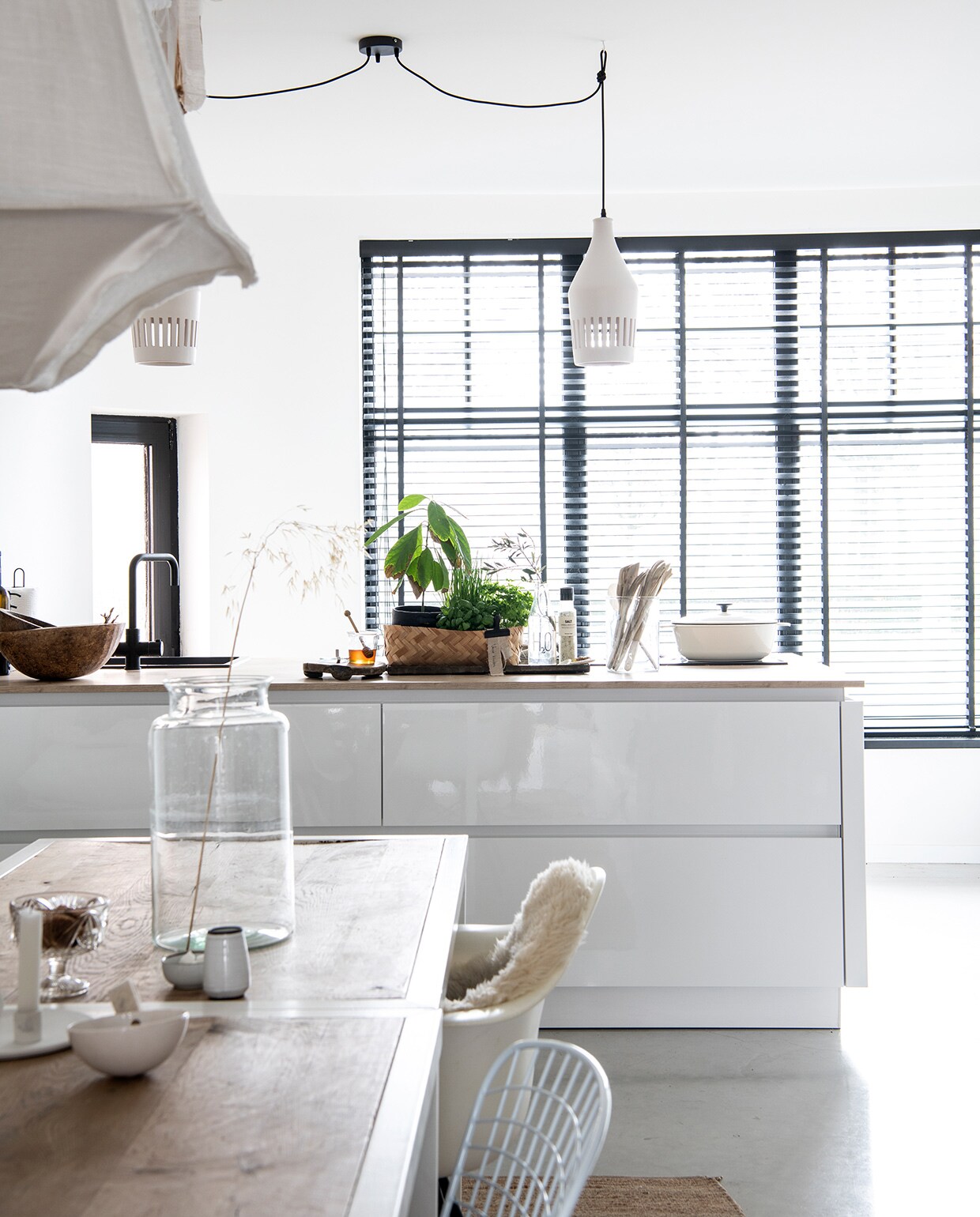 Keuken Superkeukens, raambekleding 123Jaloezie, hanglampen vtwonen. Witte pan Ikea, kraan Selsiuz via Superkeukens, houten spatels en kommen Van Hees Design, plant en plantenpot Budgetplant. Tafels uit een faillissement van een lunchroom, hanglampen vtwonen, draadstoel Jos Met Stijl, Eames-stoel Loods 5, vacht Vacht van Vilt. Kaarsen- standaard The Loving Wonen, schaaltjes en vaasjes Boet-Stijl, glazen vaas kringloop Allerhande Panningen. vtwonen 04-2021 | styling Marit Saladini | fotografie Louies Lemaire