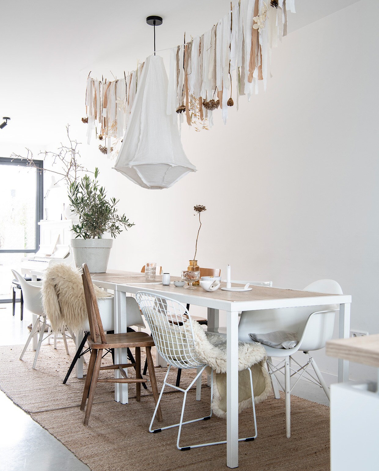 Tafels uit faillissementverkoop van een lunchroom. Draadstoel Jos Met Stijl, Eames-stoelen Loods 5, herkomst overige stoelen onbekend. Vachten op stoel en over leuning Vacht van Vilt. Kleden Wehkamp, hanglamp vtwonen, slinger Huize Jolie. Olijf in pot Budgetplant. Vaas kringloop Allerhande Panningen, kaarsenstandaard The Loving Wonen, schaaltjes, kommen en vaasjes Boet-Stijl. vtwonen 04-2021 | styling Marit Saladini | fotografie Louies Lemaire