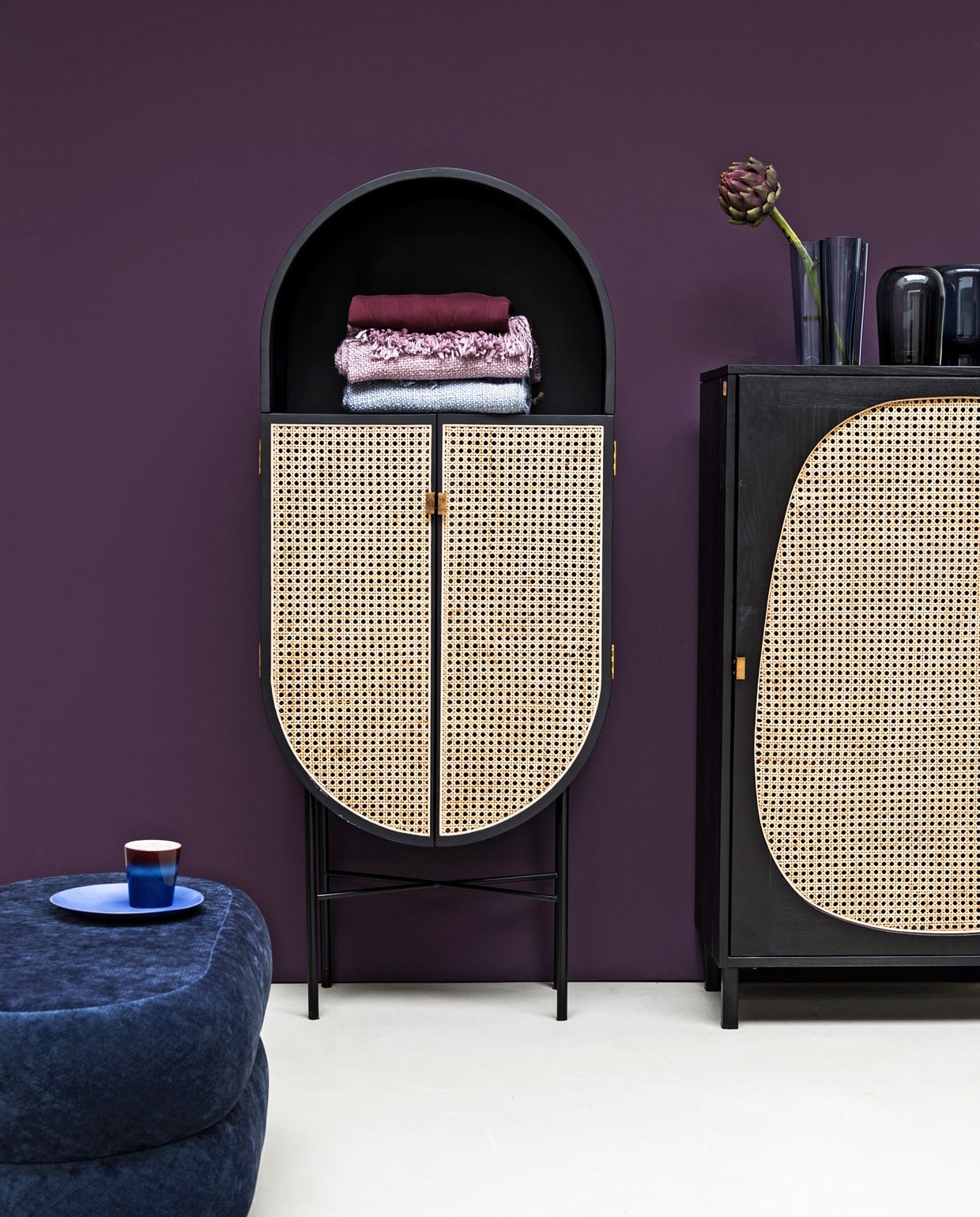 Paarse muurverf Moorland van vt wonen, (karwei.nl). Kasten Retro Oval en Retro Webbing, beide van hout, webbing en messing, blauw bord en kopje (hkliving.nl). Ovale poef van blauw velours (fermliving.com). Vaas van Ittala (links) en vaas Troll van Menu (vtwonen.nl). Plaids, (malagoon.com). Purper sweater (nike.com). vtwonen 10-2019 | Styling Marianne Luning | Fotografie Stan Koolen