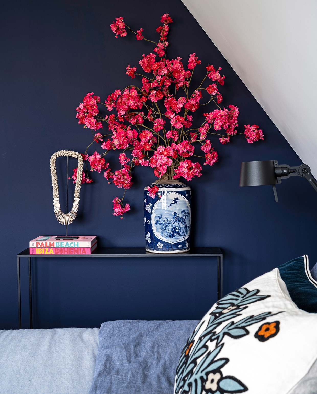 Muurverf Dock Blue 252 van Little Greene, sidetable Sissy-Boy, boeken gekregen, kralenketting Loods 5, vaas en kunstbloemen Mischa Hulshof, lamp Tonone Bolt Wandlamp Side Fit, dekbedovertrek Marco Polo, sierkussen Élitis.  vtwonen 03-2021 | productie CocoFeatures | styling Wendy Verhaegh | fotografie Stan Koolen