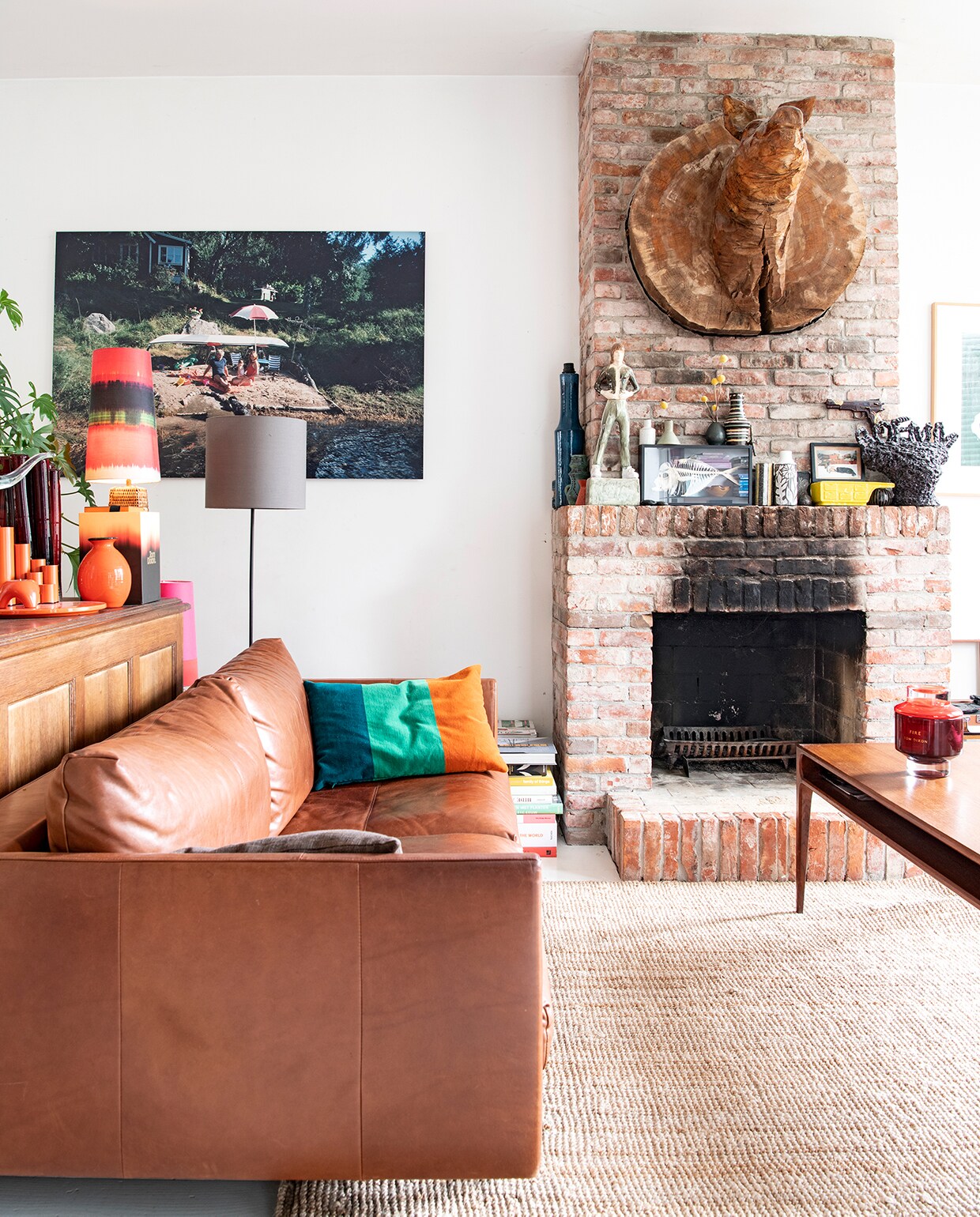 Leren bank Mobilia. Kussen, oranje vaas en door Willianne samengevoegde lampenkap en voet van de kringloop. Kunstwerk aan de muur gemaakt door Karel, vloerlamp gemaakt door Willianne. Houten varkenstorso gekocht op een festival. Op schoorsteenmantel van links naar rechts: hoge lampenvoet en vazen van de kringloop. Beeld Gerrit Jan van Ham. Ingelijste vis gekocht op kunstbeurs, erop tweede vaas van links Jonathan Adler, overige vazen erop en ernaast kringloop. Geel en grijs kunstwerk, beide gemaakt door Karel. Revolverkunstwerk Pauline Wiertz. Koffietafel uit de familie van Willianne. Kaars Tom Ford. Kleed Ikea.