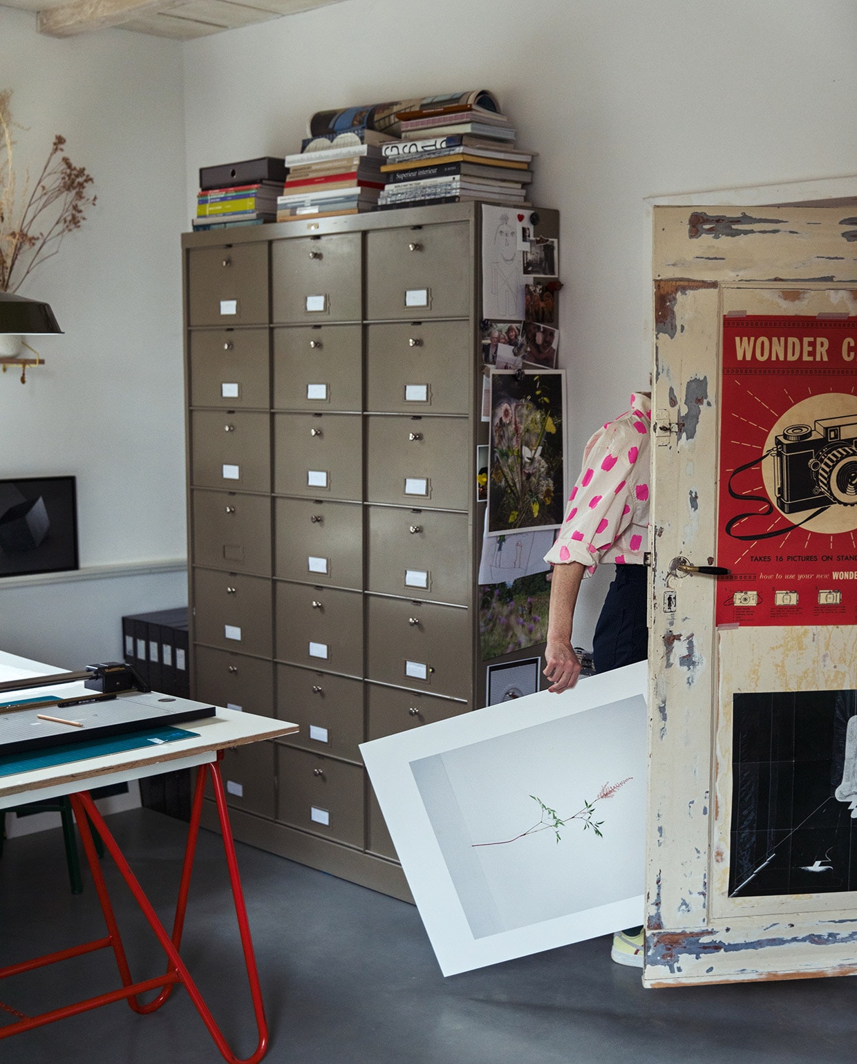 Archiefkast Neef Louis. Poster camera Vlieger Amsterdam. Bloemenfoto femkereijermanart.nl. Zwarte poster Liesbeth Abbenes. Bureau zelfgemaakt. Klapschraag bouwmarkt. vtwonen 03-2021 | Styling Ilona Jongepier | Fotografie Dana van Leeuwen | Tekst Sara Madou