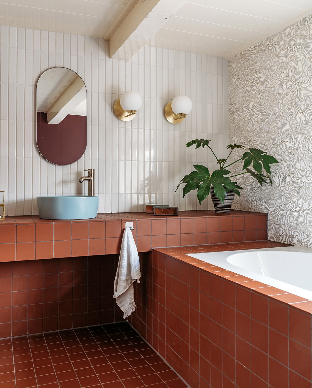 Tegels op vloer, wastafelmeubel en badombouw Vlak Rouge van Winckelmans, bovenste wandtegels Tinte Grigio Chiaro Lucido van Quintessenza. Wandlampen art deco van Flore via Lampenlicht.nl, spiegel House Doctor. Waskommen Stilo van Ben, kranen Cadans XL van Wiesbaden Sanitair. Spiegelbakje Zara Home, plantenpot kringloop. Behang Blossom Alula van Casamance. Kim heeft het twee keer met decorateursvernis van Polyvine behandeld. vtwonen 03-2021 | productie Coco Features | styling Laurien Deken | fotografie Inge Korver