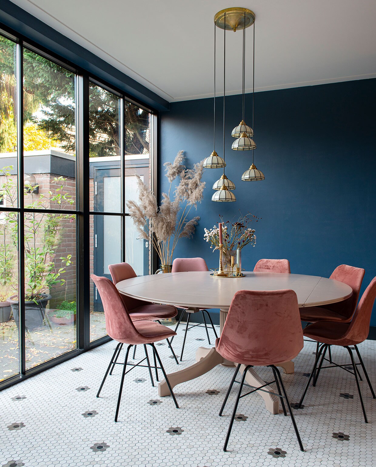Tegelvloer Designtegels. Muurverf Stiffkey Blue van Farrow &amp; Ball. Plafondverf Slaked Lime van Little Greene. Eettafel kringloopwinkel, eetkamerstoelen Kick Collection. Hanglampen Marktplaats. Grote vaas Loods 5, pampasgras zelf geplukt. Kleine vaas Jysk, bloemen zelf gedroogd. Kandelaar palmboom gekregen, gouden kandelaars en spiegelplateau Sissy-Boy, borden kringloopwinkel, mokken gewonnen bij Designtegels. vtwonen 03-2021 | fotografie Caroline Coehorst