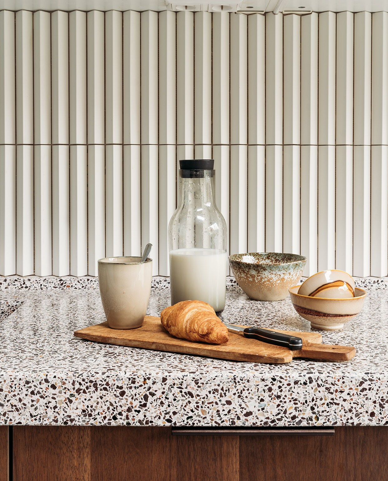Basis keuken Ikea, fronten in kleur Smoked Walnut (onder) en Kasjmiergrijs via Frontz, terrazzo blad Rosa Bian Terrazzowerken. Wandtegel Rombini triangle small white van Mutina. Plank Action, mokken Xenos, karaf Hema. Verf muur en plafond R0.10.60 van Sikkens. Stoelen Little Tulip van Artifort via Marktplaats. Tas Rough Studios. Vloer Cem-Line Micro van Loos Betonvloeren. vtwonen 03-2021 | Productie Coco Features | Styling Laurien Deken | Fotografie Inge Korver | Tekst Mariska Keus