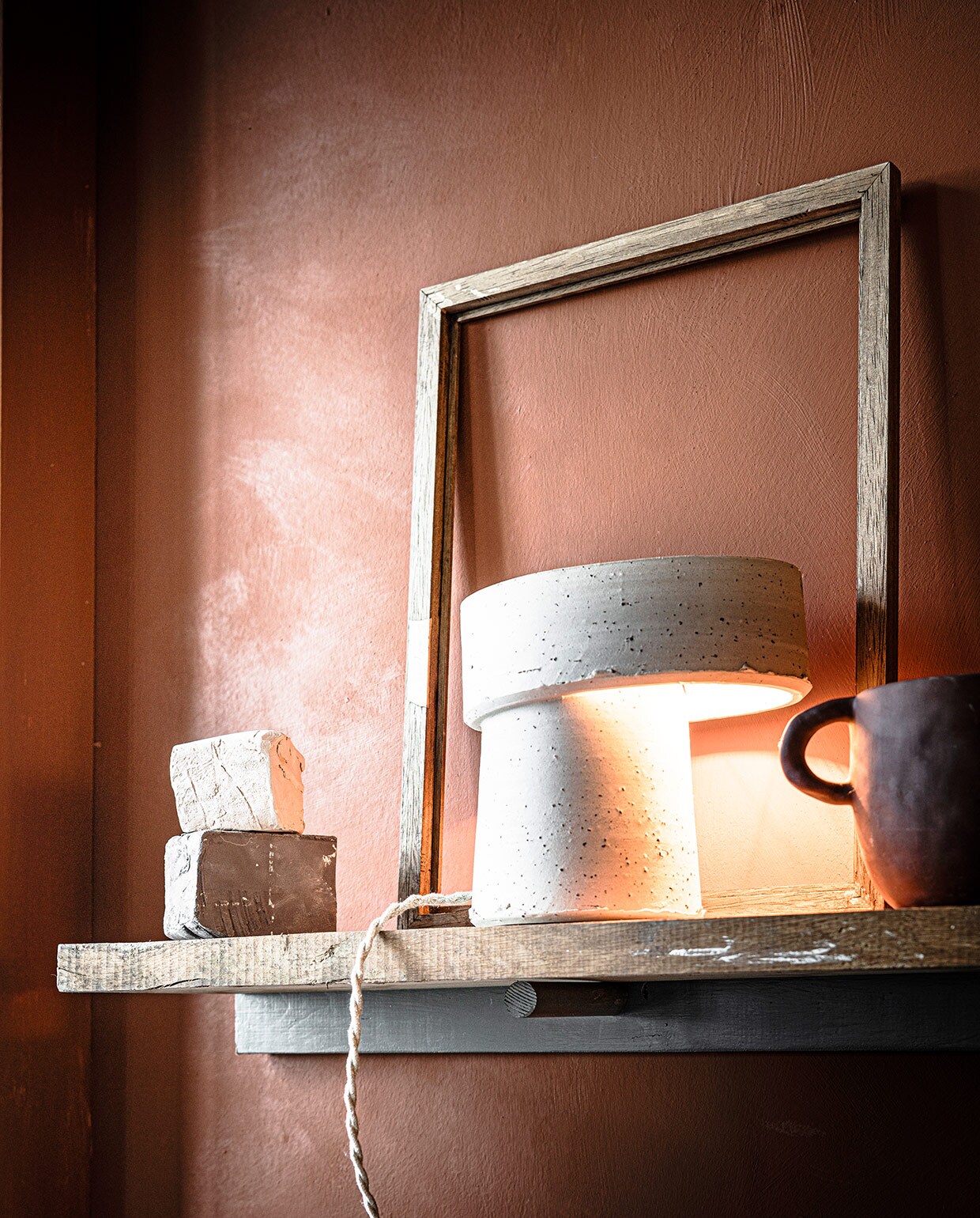 Muurverf Fresco in Terracotta (pure-original.nl). Beige lamp van klei Oysho Table Lamp (studio-yen.com). Vaas Mus Plant Pot (fermliving.com). Stukken klei (artsandcrafts.nl). Oude lijst privébezit. vtwonen 03-2021 | Styling Marlies Does | Fotografie Sjoerd Eickmans