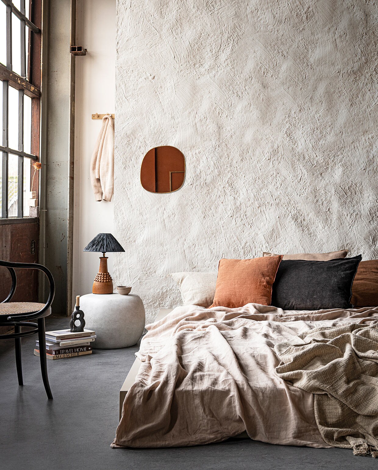 Muurverf in Chalk White (pure-original.nl). Bed op maat gemaakt en geverfd met Farrow &amp; Ball in Oxford Stone (com-anders.nl). Linnen dekbedovertrek in Sand van Linge Particulier, kussen Sabra offwhite Oblong XL, linnen kussenVice Versa van Maison de Vacances, kussen Vice Versa Canvas Formentera van Maison de Vacances, kussen Vice Versa Toile Nomade van Maison de Vacances, messing spiegel Ame van Caravane (couleurlocale.eu). Zwart kussen van vtwonen collectie (vtwonen.nl). Bijzettafel Pebble van vtwonen collectie (basiclabel.nl). Lamp van Madam Stoltz (deens.nl). Kandelaar van Malwina Kleparska, boek van Bea Mombaers (studio-yen.com). Kom van klei (household- hardware.nl). Kapstok van ByOn (littledreamers.nl). Stoel en overige boeken privébezit. vtwonen 03-2021 | Styling Marlies Does | Fotografie Sjoerd Eickmans