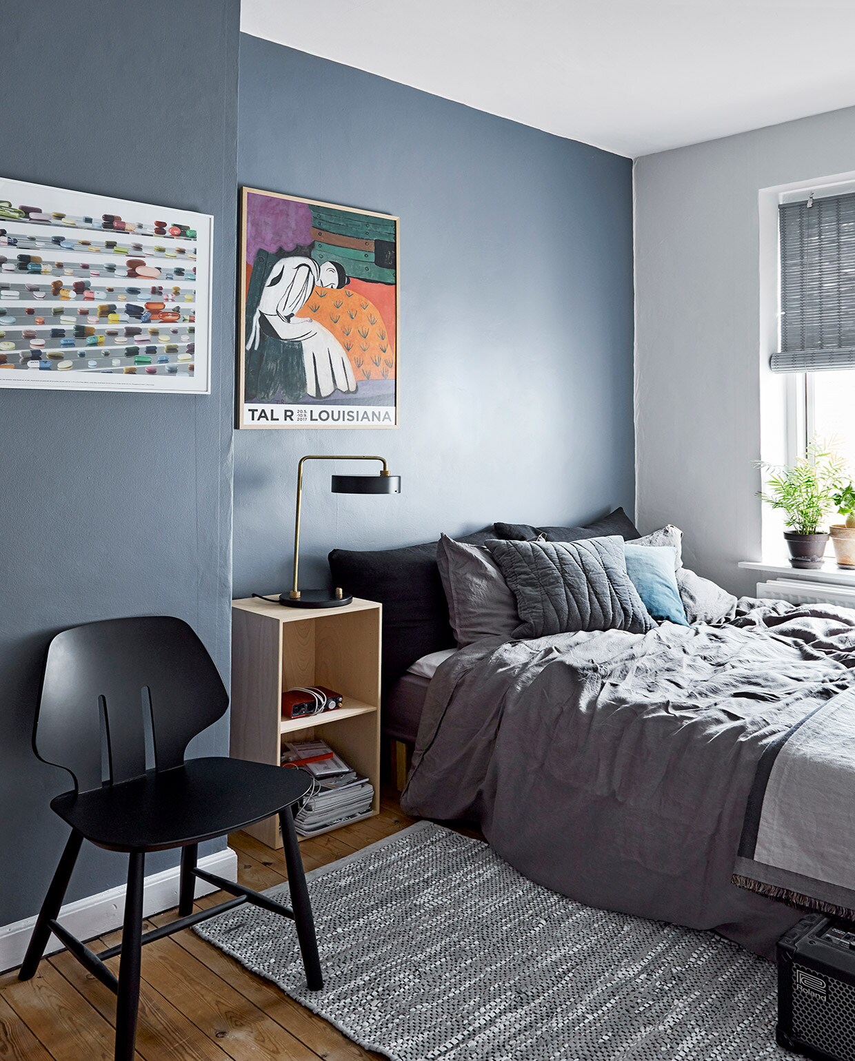 Muurverf 4618 Evening Sky van Jotun. Bamboe gordijn Color &amp; Co, bed Ikea, grijs beddengoed H&amp;M, grijs fluwelen kussen Linnum. Herkomst nachtkastje onbekend. Tafellamp Made by Hand, zwarte stoel J67 van Fdb Møbler, vloerkleed Rug Solid. Kunstposter Tal R uit Louisiana Museum of Modern Art, poster Damien Hirst uit Tate Gallery London. vtwonen 02-2021 | Productie en fotografie Stine Christiansen | Styling Gitte Christensen