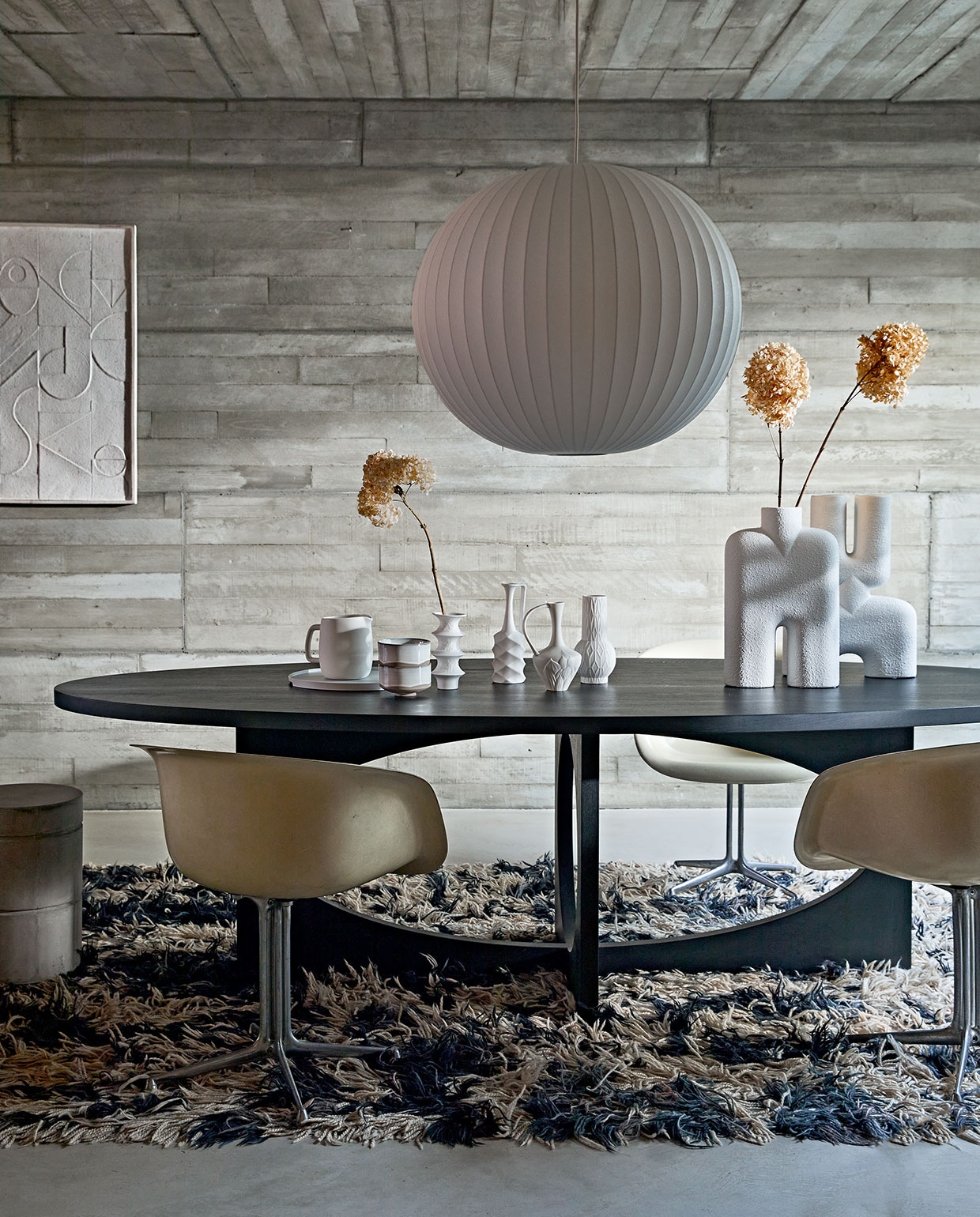 Zwartgebeitste massief eikenhouten ovale tafel van ontwerper Sarah Trenite, 260x115x75 cm (lxbxh), prijs op aanvraag (arpdesign.com). Vintage La Fonda kuipstoel van Eames voor Herman Miller, prijs op aanvraag (pietjonker.nl). Grote witte vazen Cobra Bubble tall € 120,- en Double Bubble tall € 135,- van 101CPH (edha-interieur.nl). Schilderij met reliëf, 100×70 cm € 199,- (urbannatureculture.nl). Kleine vazen van HKliving, set van 4 € 129,95, keramieken waterkan van ontwerper Vincent van Duysen voor Serax, 1,5 liter € 25,-, hanglamp Nelson Ball Bubble van Hay, 68 cm (Ø) € 607,99, dienblad van Zone Denmark, 35 cm (Ø) € 50,-, kommen Merci n°1 van Serax, 12,5 cm (Ø) per stuk € 16,65 (vtwonen.nl). Betonnen kruk van Marie Michielssen, 30×45,5 cm (Øxh) € 103,- (serax.com). Gedroogde hortensia’s (edenique.nl). Soortgelijk vintage vloerkleed (vintagehoarder.com). vtwonen 02-2021 | Styling Cleo Scheulderman | Fotografie Jeroen van der Spek