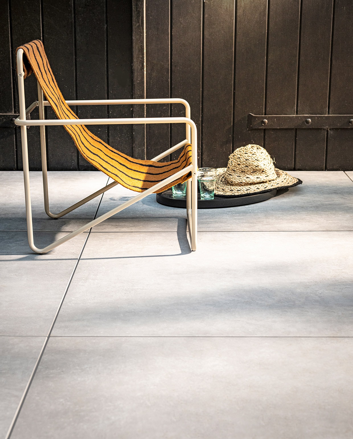 Tegel Solostone Uni Mold Grit, , 90x90x3 cm (lxbxh) per m² € 80,- (ook verkrijgbaar in Basalt, en in Grit, Basalt en Taupe in 70x70x3,2 cm). M.m.v. kolkenkolk.nl (Desert Lounge Chair kids van Ferm Living), vtwonen.nl (dienblad van Serax), householdhardware.nl (glazen). Overig privébezit. vtwonen 03-2021 | Productie Tanja Saarberg | Styling Kim van Rossenberg | Fotografie Sjoerd Eickmans\n