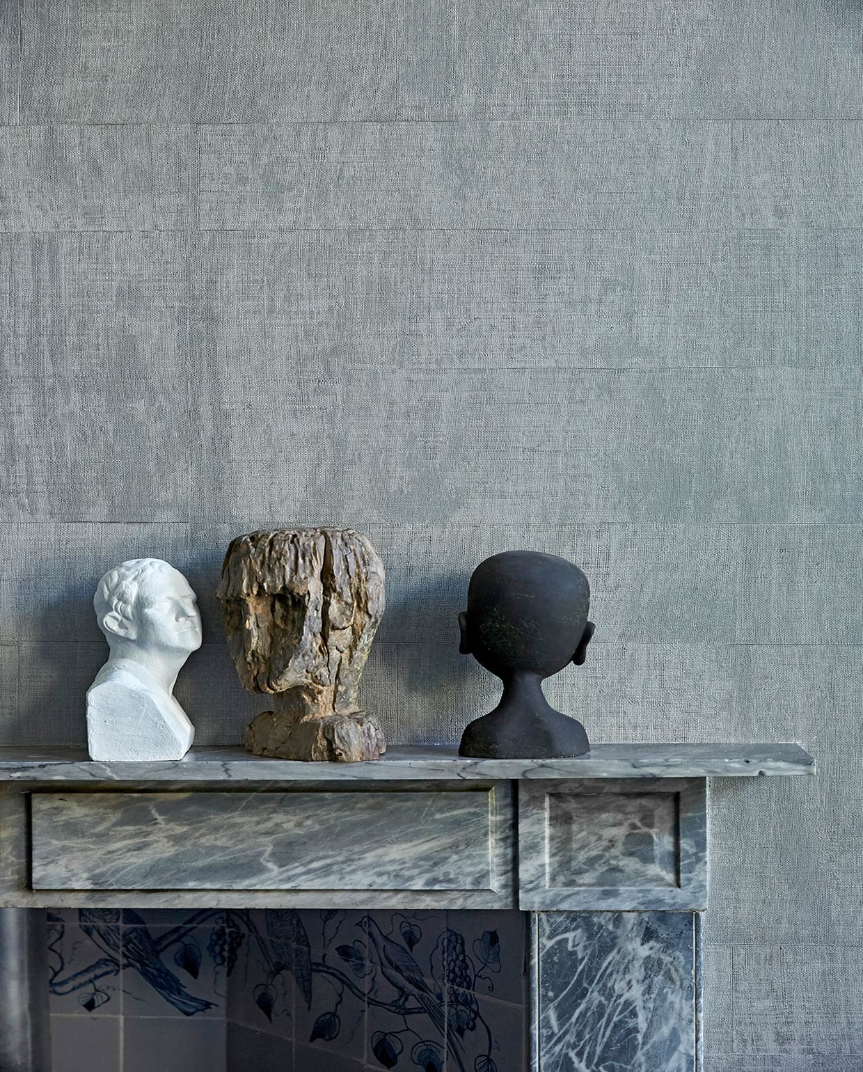 Grijs behang op muur Atelier d’Artiste Elitis via Loggere Wilpower. Marmeren schouw originele Rococo-schouw. Witte buste van een winkel die niet meer bestaat, antieke houten buste uit India, zwart hoofd van GMC uit Zuid-Afrika. vtwonen 02-2021 | fotografie Tjitske van Leeuwen | styling Marianne Luning