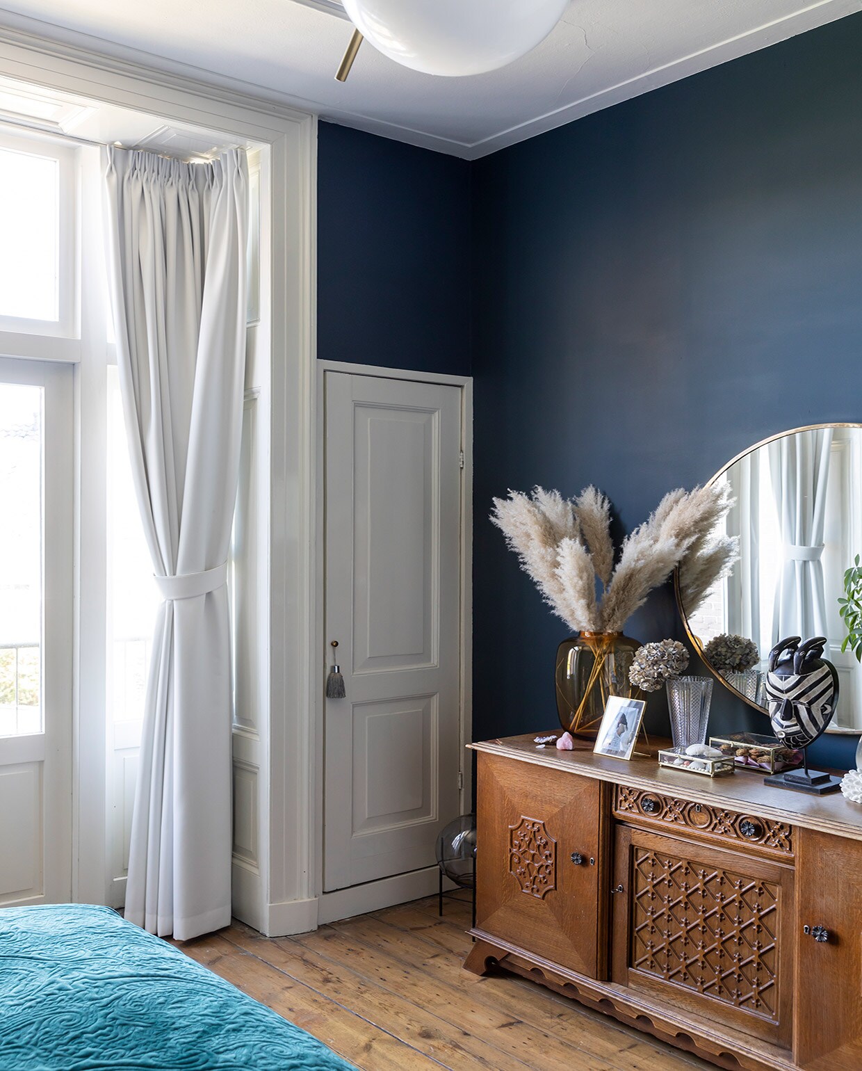 Muurverf Hague Blue Farrow &amp; Ball, originele vloer uit 1889, hanglamp Flos, bed Auping, nepplant Strelitzia en pot Jasmijn Bloembinders, wandlamp Karwei, blauwe vaas HKliving, vogel Toikka Iittala, fotolijst van Christians ouders geweest, beddengoed bloemenprint, wollen plaid, paars kussen en rond kussen Essenza. vtwonen 01-2021 | Productie en Fotografie Margriet Hoekstra | Tekst Anna van der Heijden