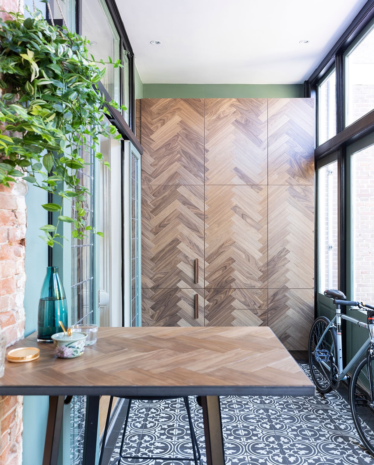 Hoge bartafel onderstel van Hay met massief eikenhouten blad gemaakt door SkillsXL, blauwe waterkan en waterglas Ikea, Portugese vloertegels Designtegels. vtwonen 01-2021 | Productie en Fotografie Margriet Hoekstra | Tekst Anna van der Heijden