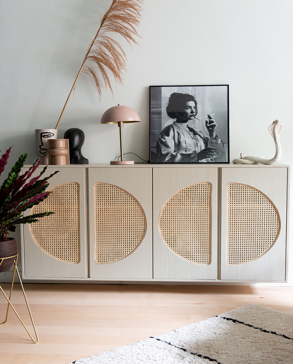 Kast , zelf cirkels uitgefreesd en met pitriet omgebouwd tot webbingkast, geverfd met van Farrow &amp; Ball. Vaas gezicht  voorste vaas en object gezicht . Lamp  Portretfoto van buurjongen gekregen. Beeld cobra vintage vondst. Plantenstandaard  plant Calathea. Vloerkleed , bankhoes . Muurverf verkeerswit Ral 9016. vtwonen 01-2021 | Styling Jeske Weel | Fotografie Caroline Coehorst \n\nvtwonen 01-2021 | kastjes met webbing, schilderij van meisje aan het roken, roze lamp