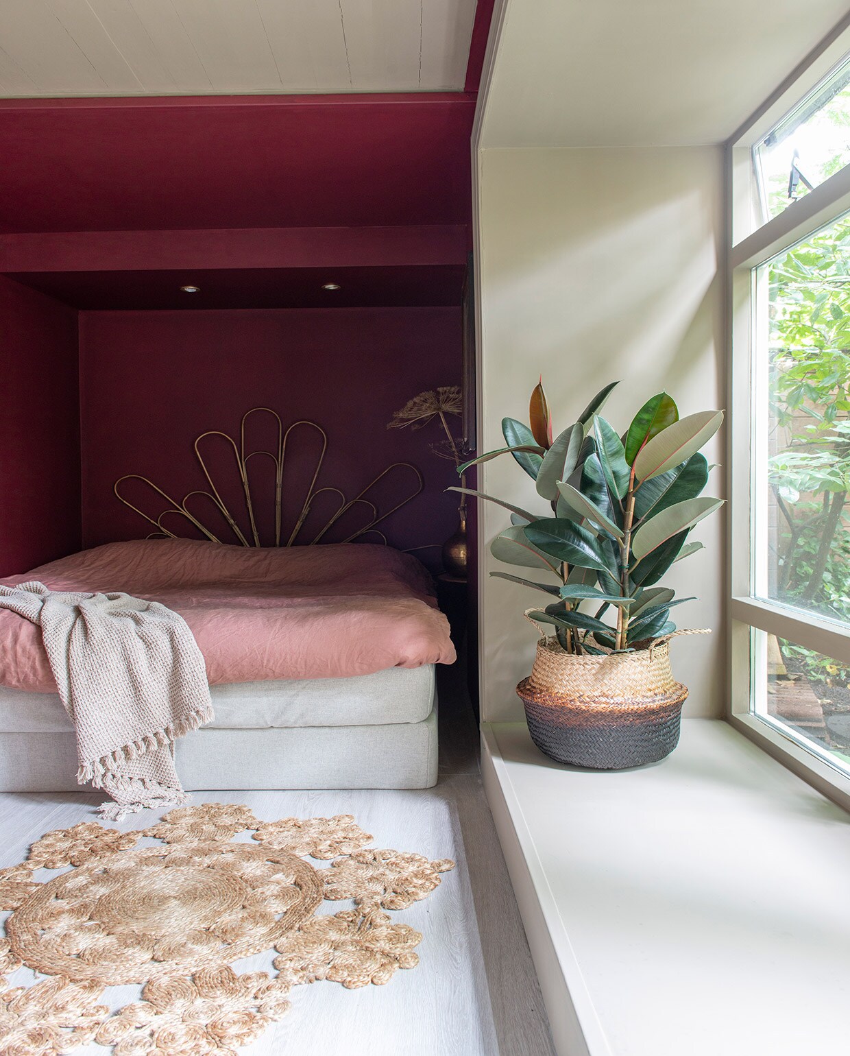 Muurverf en lakverf  van Farrow &amp; Ball. Bed . Achterwand zelfgemaakt van bamboe plantensteunen. Kussen en plaid  Mand , erin een rubberplant. Laminaatvloer restpartij van een winkel die niet meer bestaat. Vloerkleed garage sale. Bijzettafel , herkomst pot onbekend, tak gedroogde berenklauw. vtwonen 01-2021 | Styling Jeske Weel | Fotografie Caroline Coehorst