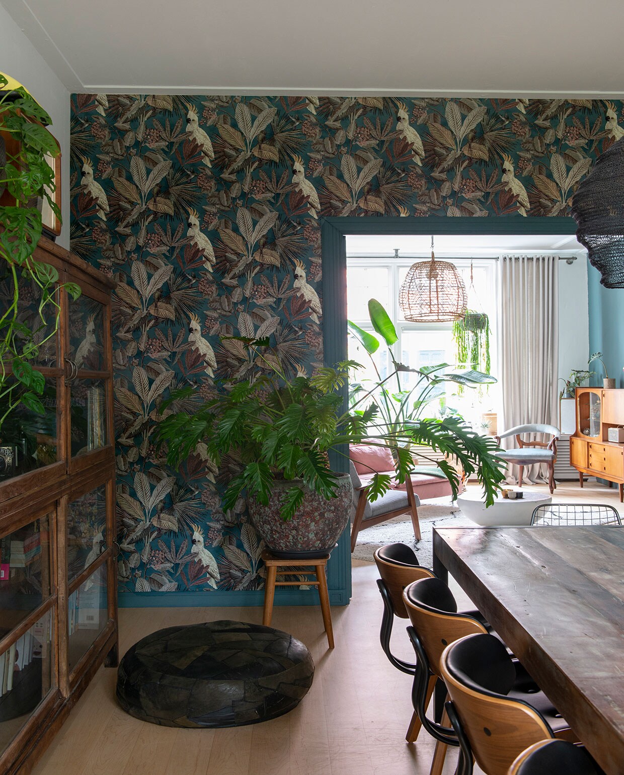 Bank en grijze fauteuil , bankhoes Norsemaison. Groene plaid, kandelaars op tafel  Vloerkleed . Salontafel van een designveiling. Plafondlamp . Platenspelermeubel, vaas op schouw, blauwe stoel en kast vintage vondsten, soortgelijke kast @trashuresnl. Plantenpot met cactus op schouw . Zwart beeld en minivaas aan muur vintage Cortendorf. Vintage pot met hangplant String of hearts. Muur- en lakverf van Farrow &amp; Ball. Grote plant Strelitzia, pot . De esdoornhouten vloer lag er al. Gordijnen . Behang Toekan , plant ervoor vingerplant. Paneeldeuren Stichting Monument &amp; Materiaal. vtwonen 01-2021 | Styling Jeske Weel | Fotografie Caroline Coehorst