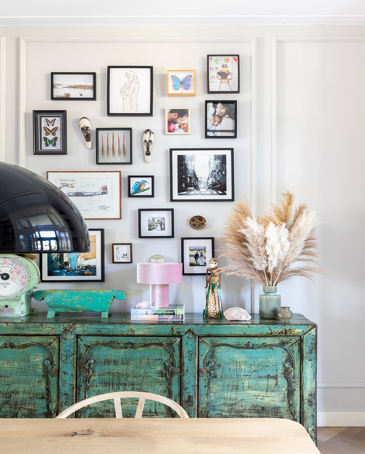 Dressoir uit Indonesië via Bij Jasmijn, tafel zwaartafelen.nl, stoelen Wishbone Chairs van Carl Hansen. Op dressoir: kleine pot Dekatuin, oude scheepsklok en groen houten kunstwerk uit Bali, roze lamp Westwing, Indonesische pop kringloop, vaas Made, minivaas van Christians oma geweest. Aan muur: fotolijsten Ikea en kringloop, maskers uit Zuid-Afrika, vlinders Anna + Nina en All the luck in the world, foto’s gemaakt door Natalia van der Zalm en Kee &amp; Kee, kunstwerken uit New York (vierkant), een atelier in Zwolle (ijsvogel) en cadeau gekregen. NEE vtwonen 01-2021 | Productie en Fotografie Margriet Hoekstra | Tekst Anna van der Heijden